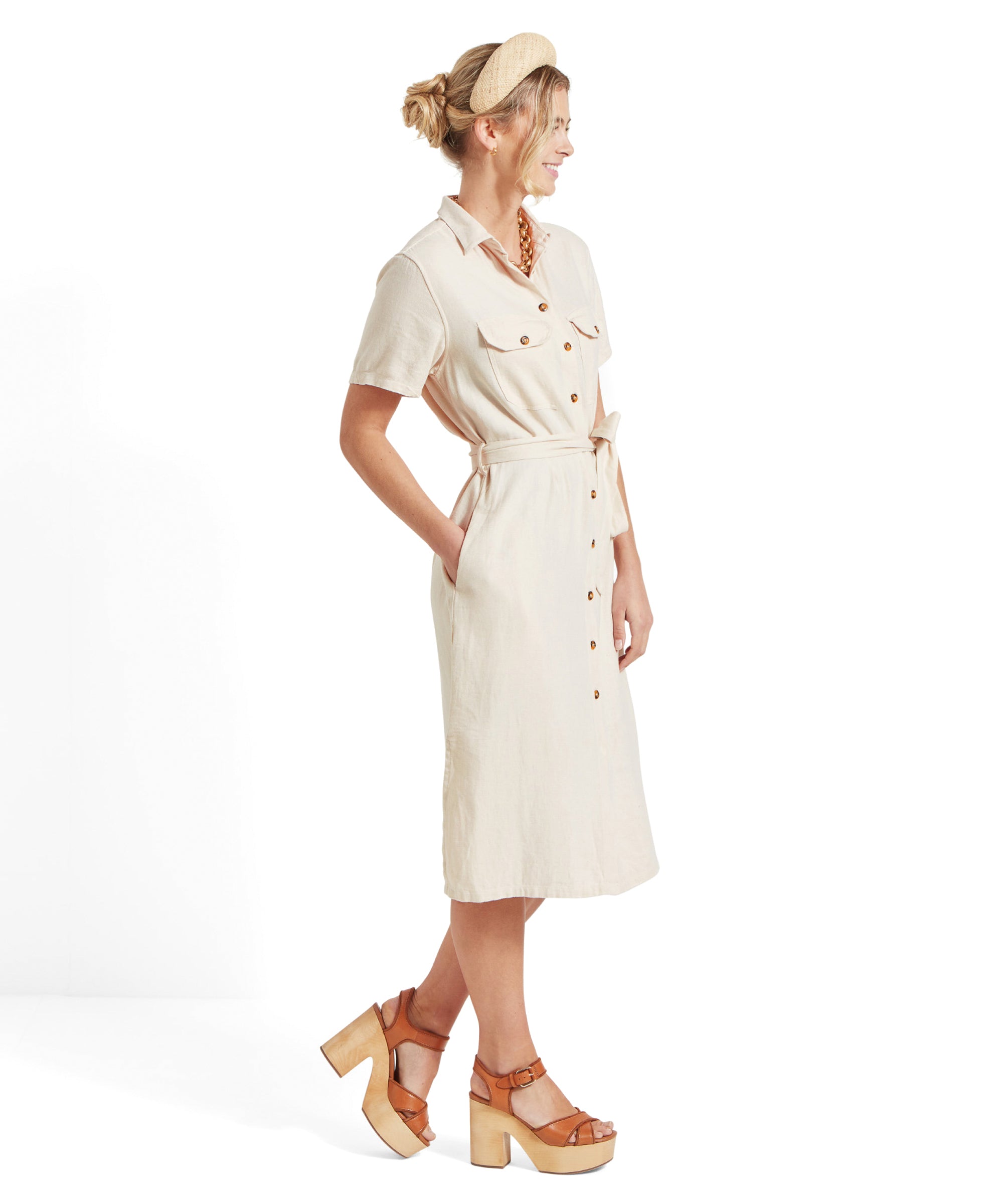 Side view of the woman wearing Schöffel Daisy Linen Dress for Women in Light Brown, highlighting the pockets and waist tie, while she is smiling and looking forward.