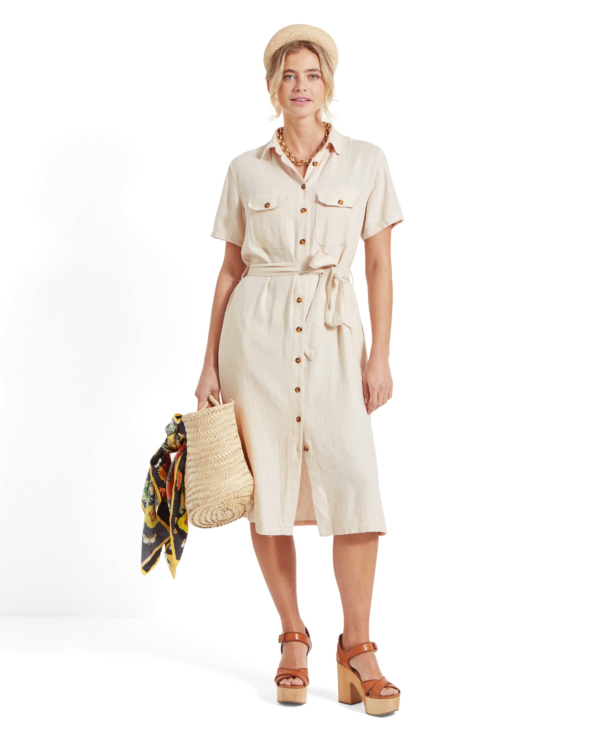 Front view of the woman, slightly closer, focusing on her holding the straw bag, highlighting Schöffel Daisy Linen Dress for Women in Light Brown buttons and her accessories.