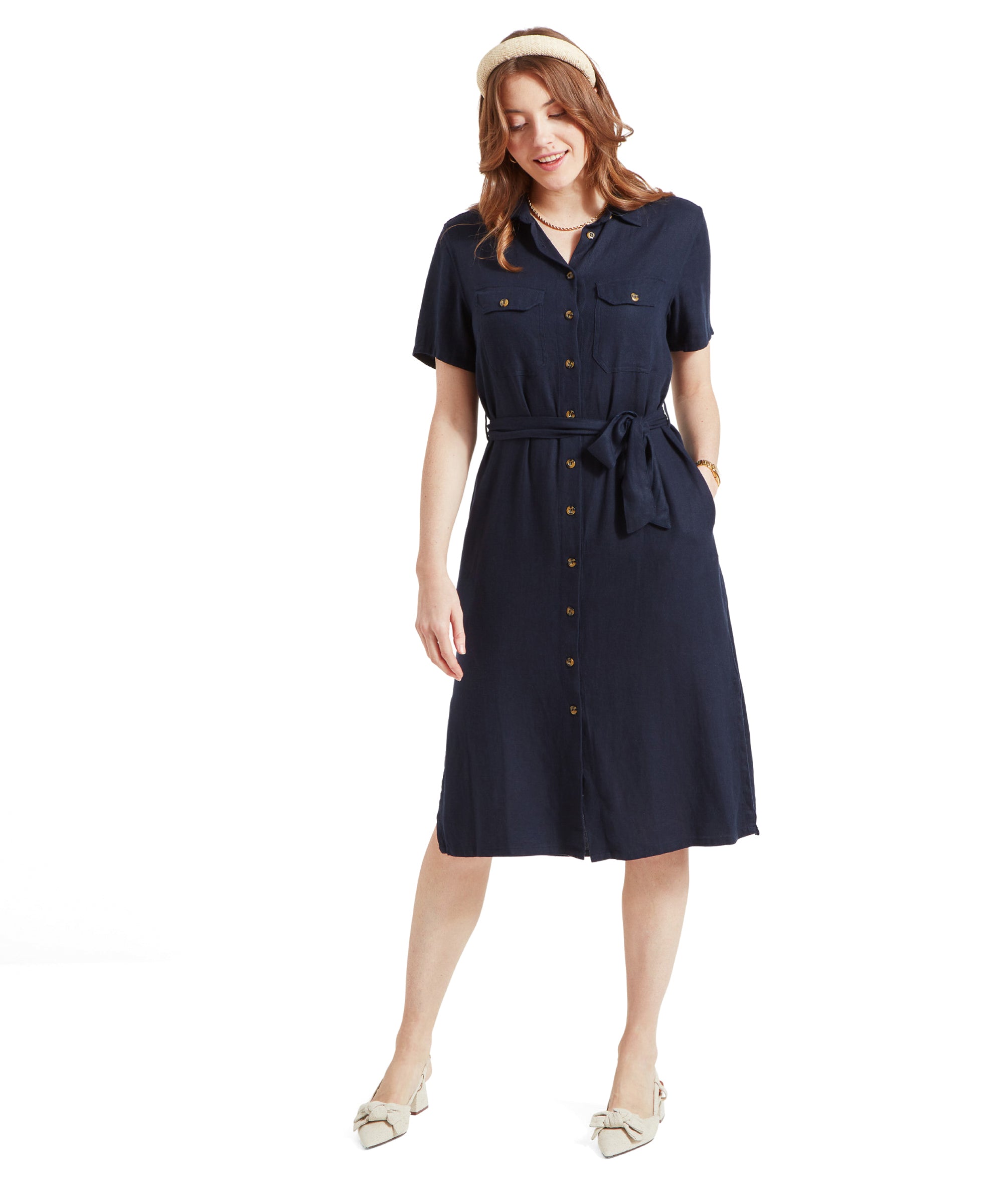 Woman wearing Schöffel Daisy Linen Dress for Women in Navy with short sleeves, front button closure, and a waist tie, standing and looking down.