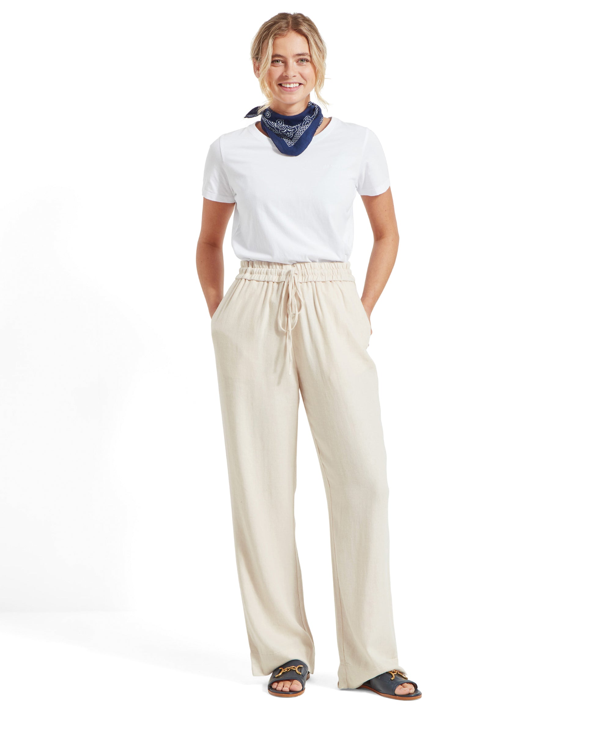 The same Schöffel Daphne Trousers for Women in Light Brown, paired with a white t-shirt and a blue bandana around the neck, hands in pockets.