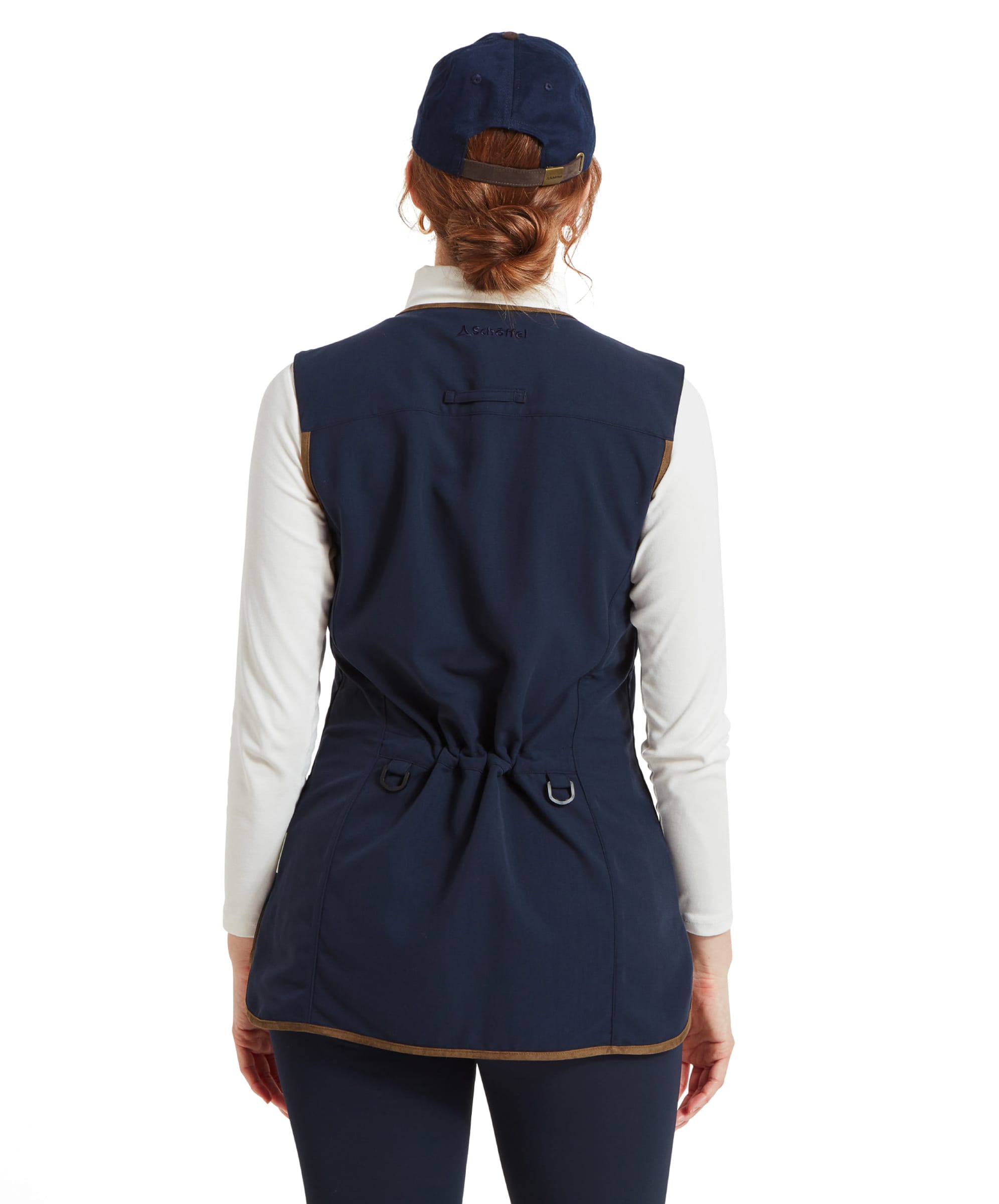 A rear view of the woman wearing the Schöffel Edenham Clay Shooting Vest for Women in Blue, showing the adjustable back with drawstrings. She is standing with her back facing the camera, her hair tied back under a navy cap.