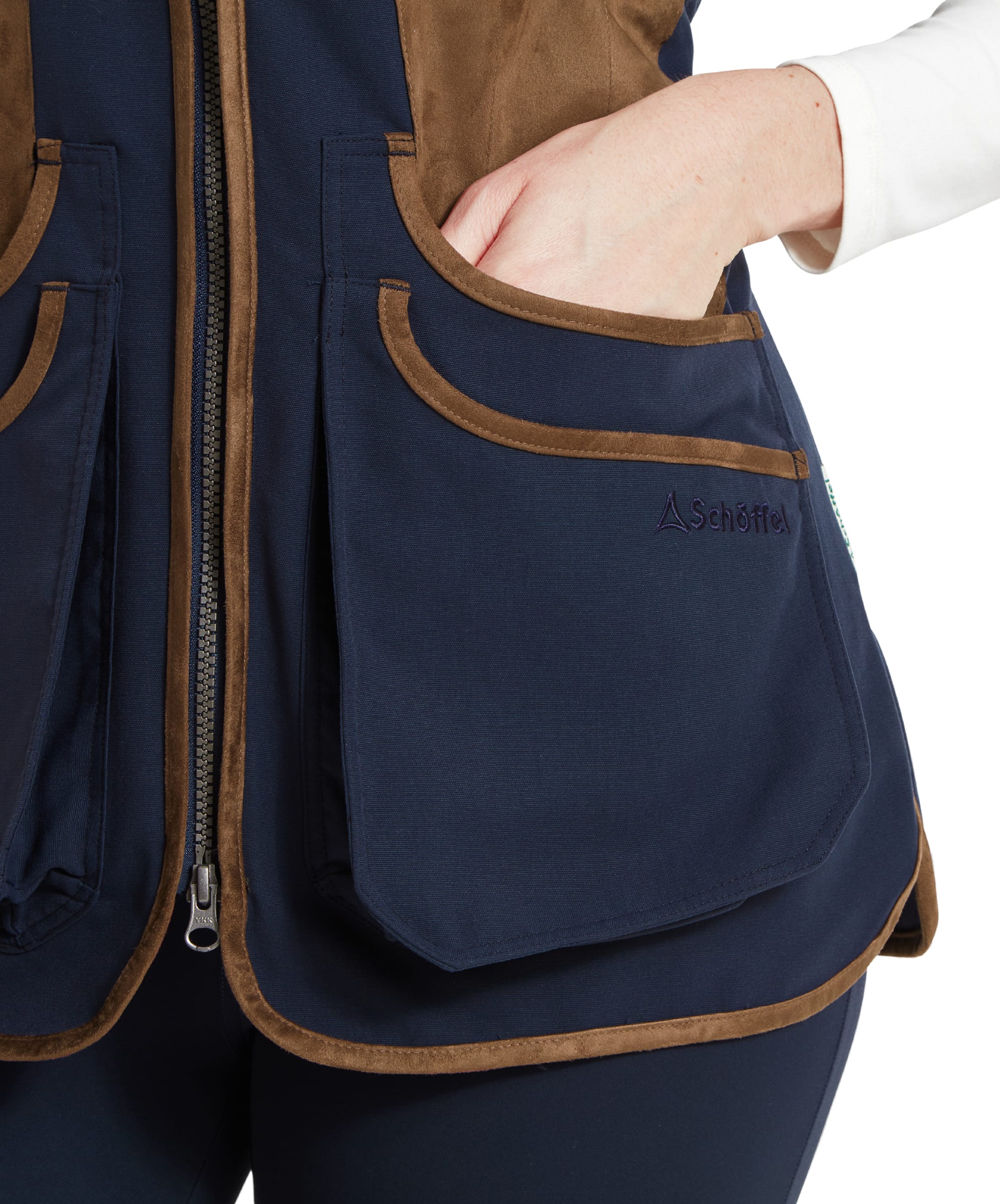 A close-up of the Schöffel Edenham Clay Shooting Vest for Women in Blue’s front pocket with the woman's hand partially inserted. The vest is brown and navy blue, with detailed piping around the pocket edges.