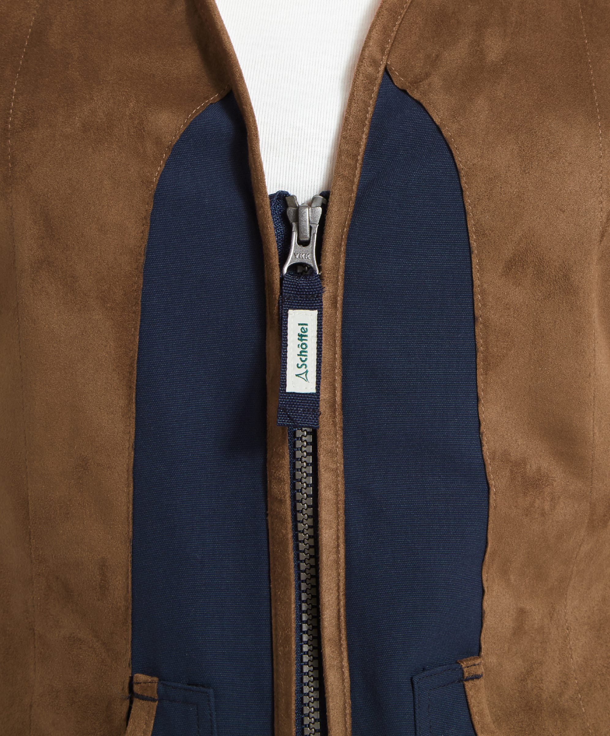 A close-up of the front of the Schöffel Edenham Clay Shooting Vest for Women in Blue, focusing on the zippered front with a Schöffel-branded zipper pull. The material shows a contrast between the brown and navy blue sections.