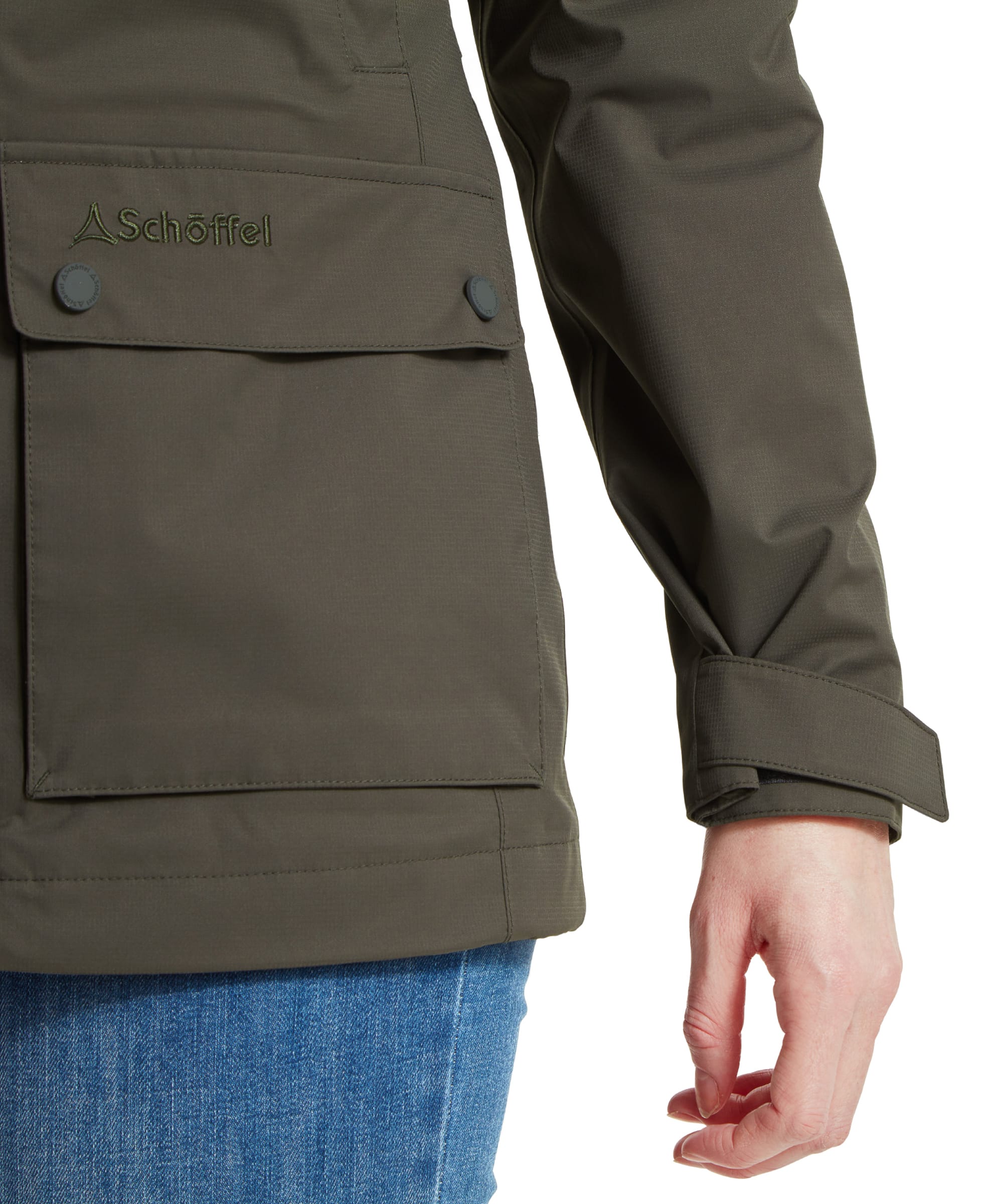 Close-up of the lower section of the Schöffel Edith Jacket for Women in Green, showing the Schöffel logo embroidered above the buttoned pocket flap. The jacket features an adjustable cuff strap.