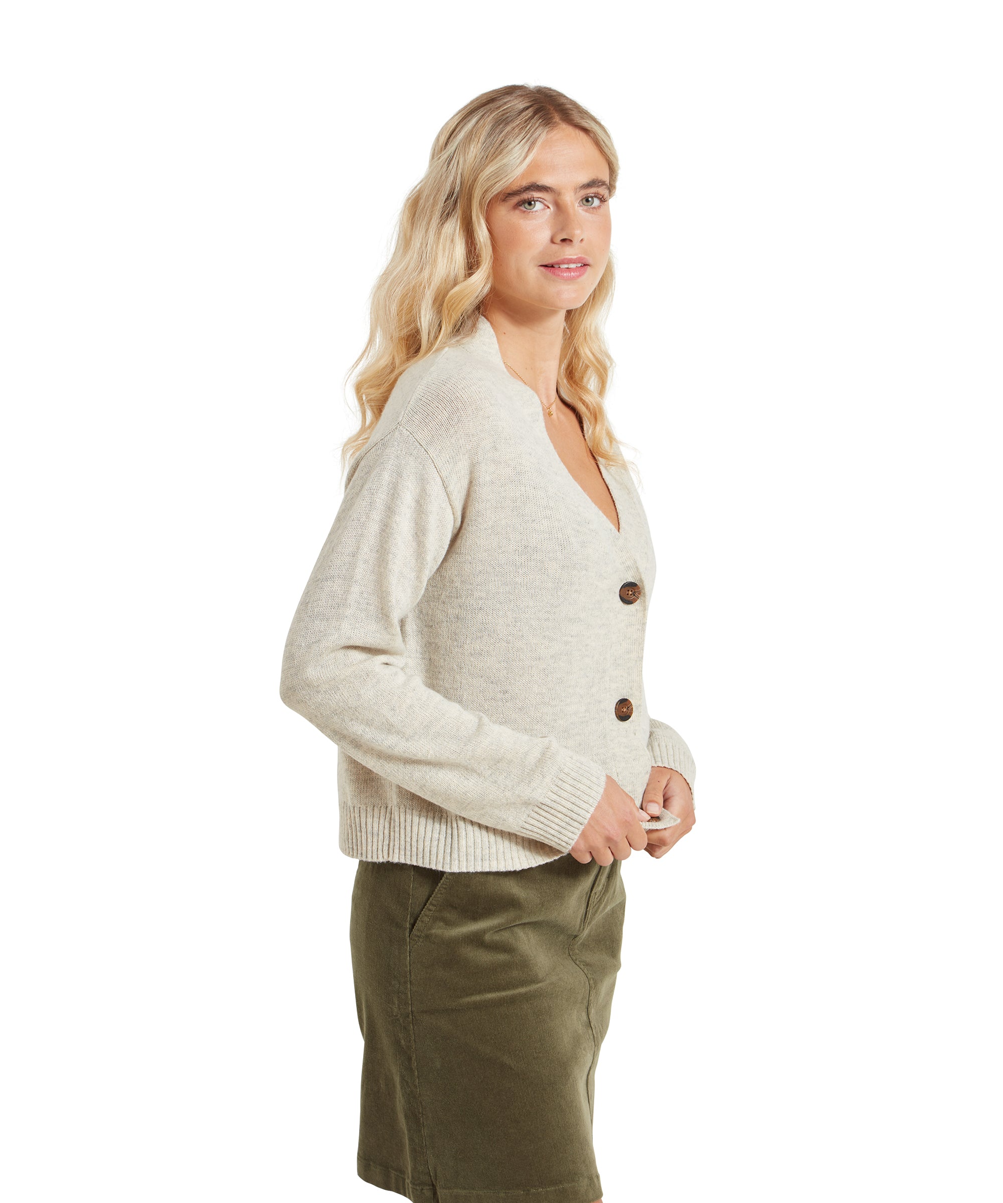 A side profile of the woman wearing the Schöffel Filey Cardigan for Women in Beige, showing the fit and style from the side view. She still wears the olive green skirt.