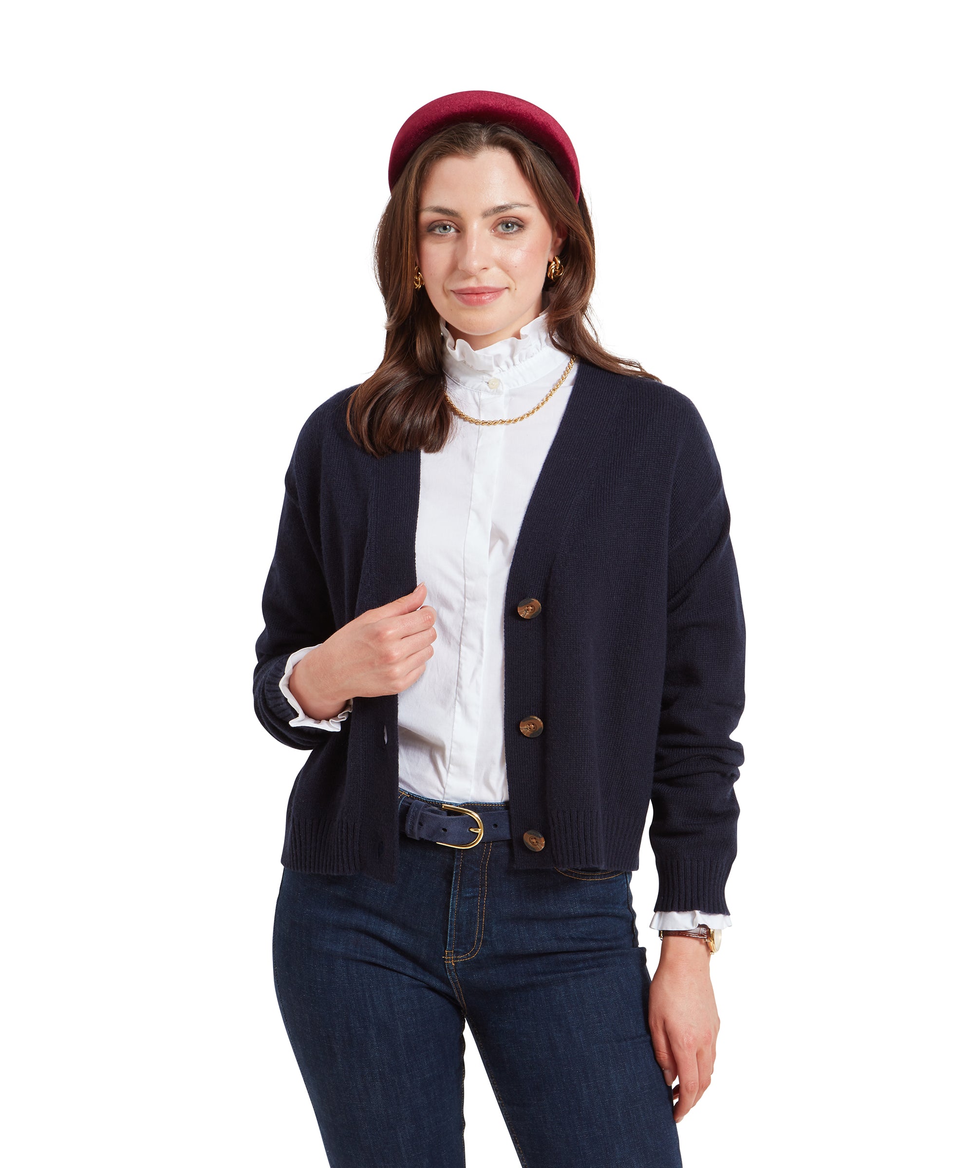 A woman wearing a Schöffel Filey Cardigan for Women in Navy with brown buttons, a white shirt with a ruffled collar, and jeans. She accessorises with a red headband and gold earrings, looking slightly off to the side.