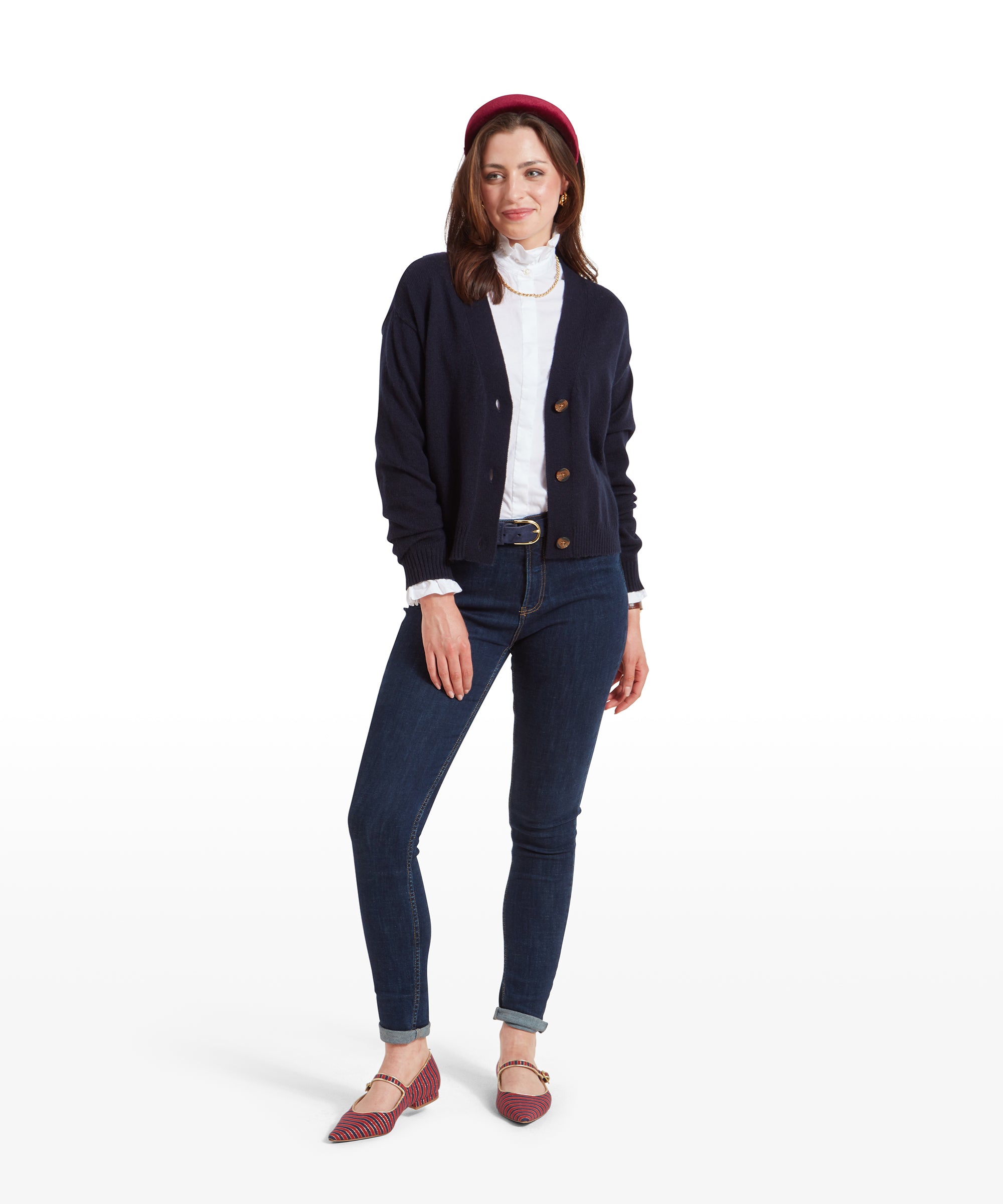 The same woman standing fully, showcasing the Schöffel Filey Cardigan for Women in Navy, white ruffled shirt, jeans, and red flats. She poses with one hand on her hip, smiling slightly.