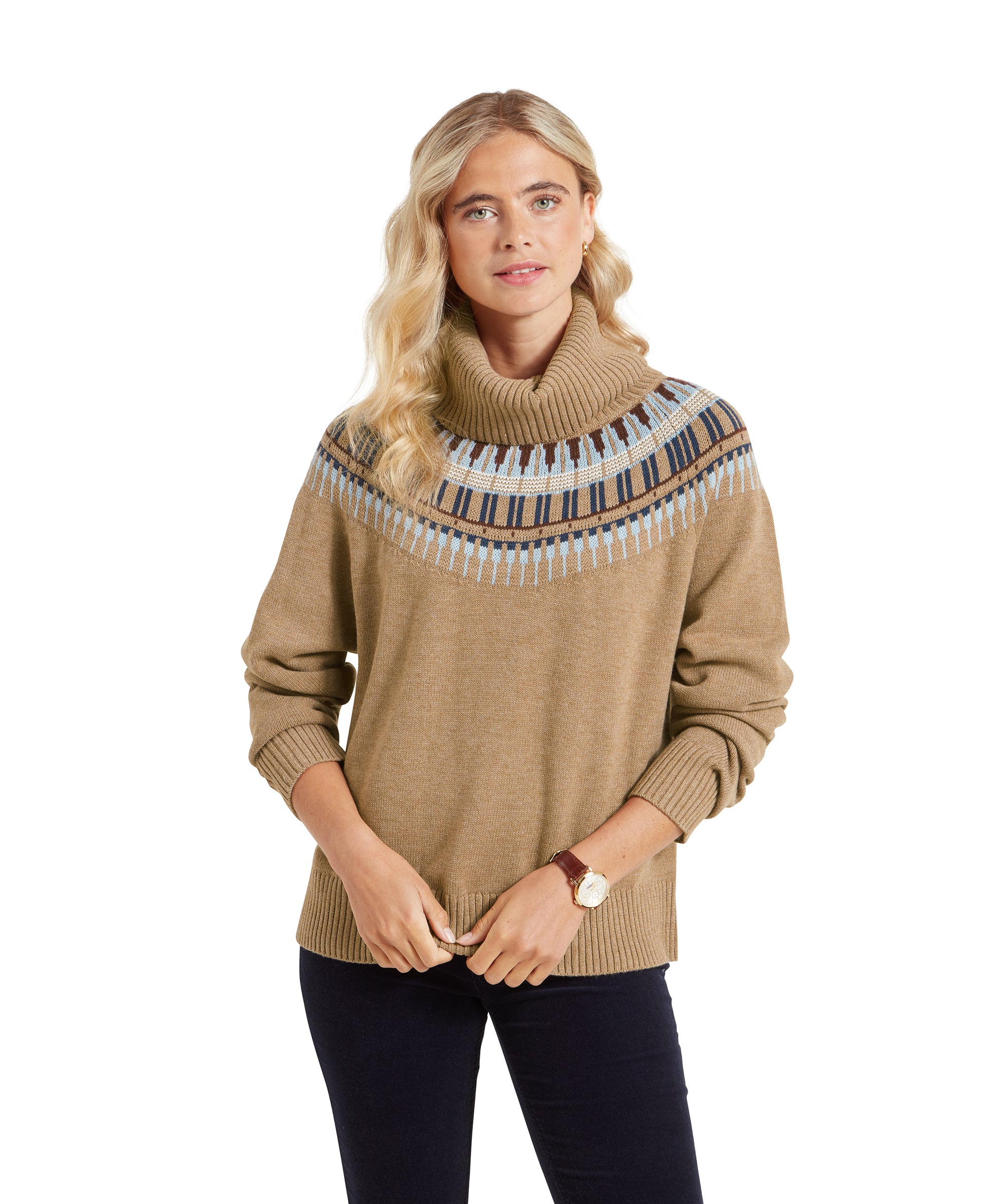 A woman wearing a Schöffel Filey Fairisle Roll Neck Jumper for Women in Beige Fair Isle pattern across the shoulders. She is standing with her hands lightly clasped in front of her, looking directly at the camera with a soft smile. The jumper has a cozy, relaxed fit, paired with dark trousers.