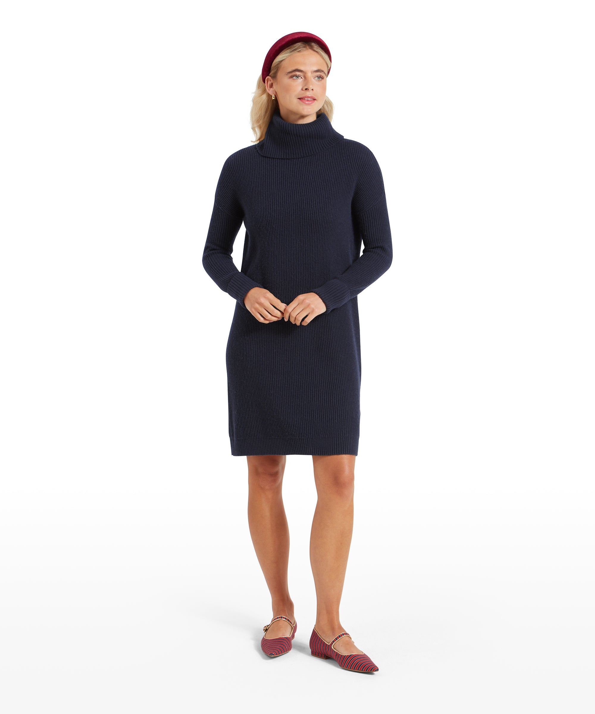 The same woman in a full-body shot, standing with her hands together in front of her, showcasing the Schöffel Filey Roll Neck Dress for Womens in Navy. She is wearing the same burgundy headband and red striped flats.