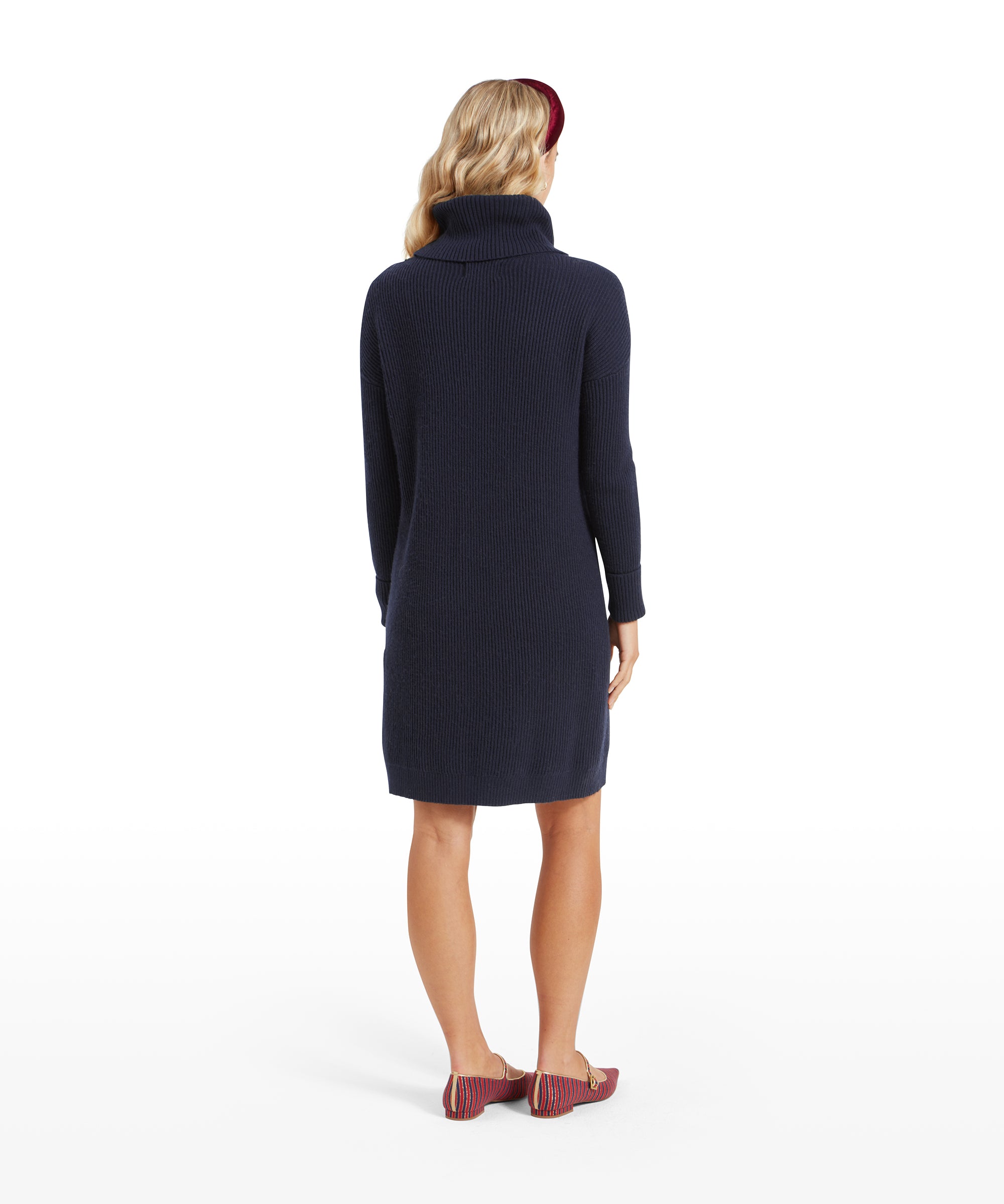 The woman is seen from the back, showing the back details of the Schöffel Filey Roll Neck Dress for Womens in Navy, with her head turned slightly to the side. She continues to wear the burgundy headband and red striped flats.