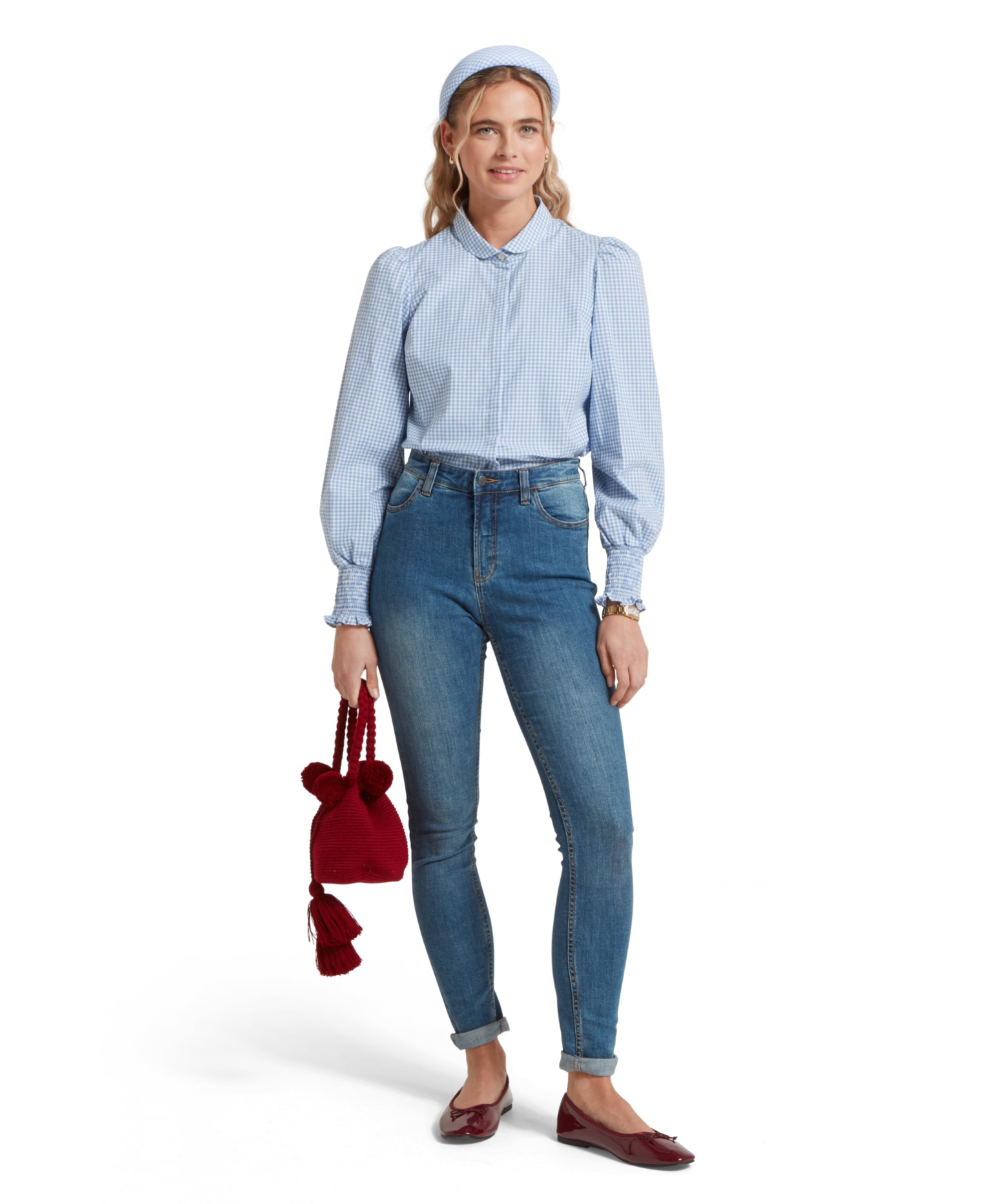 Full height image of a female model wearing a blue and white gingham Schöffel shirt, tucked into a pair of mid wash denim jeans, paired with red leather pumps a red handbag.