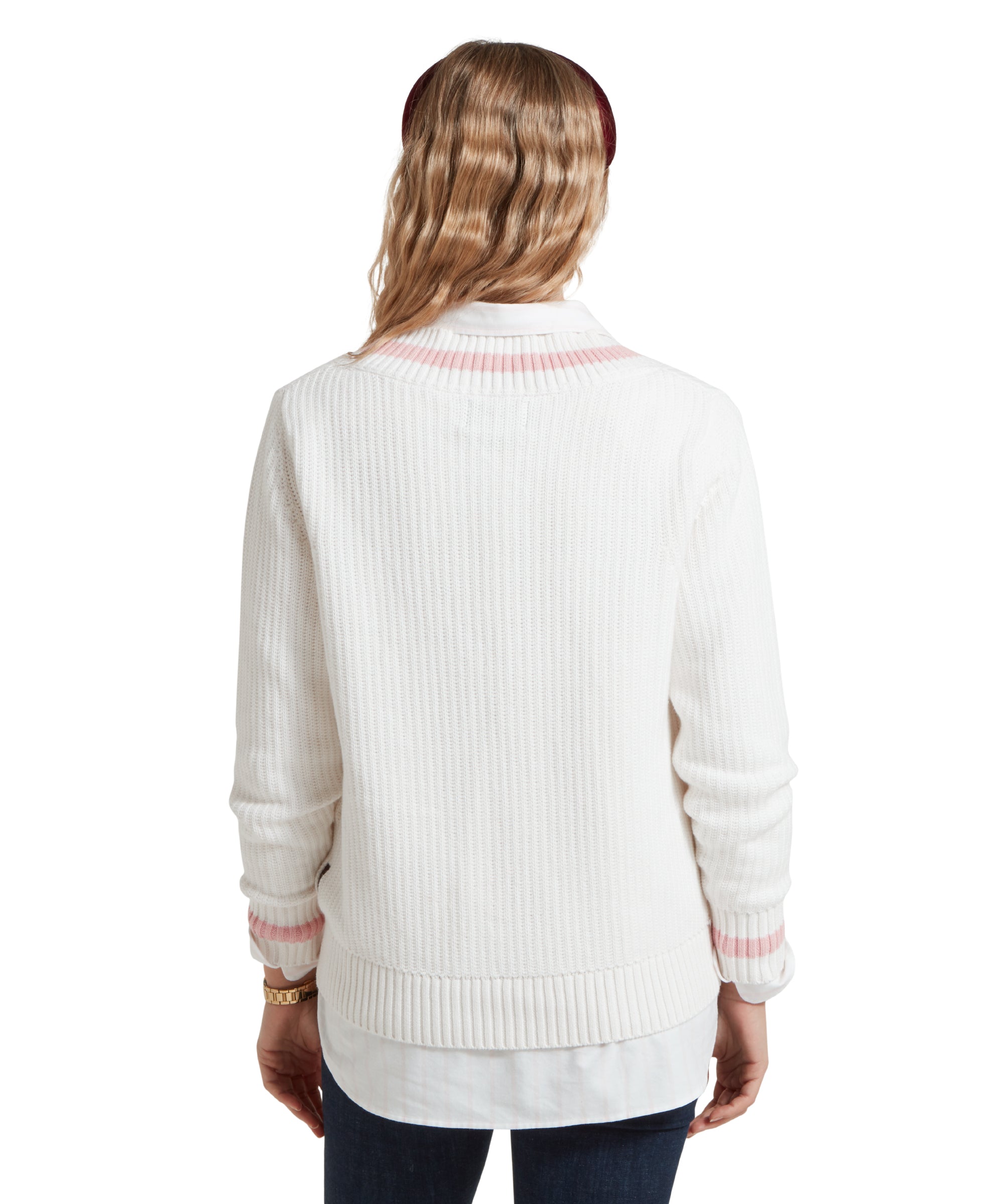 A back view image of a female model wearing a white Schöffel jumper with pink trim on V-neck collar and cuffs, paired with a white shirt, dark denim jeans and red headband.