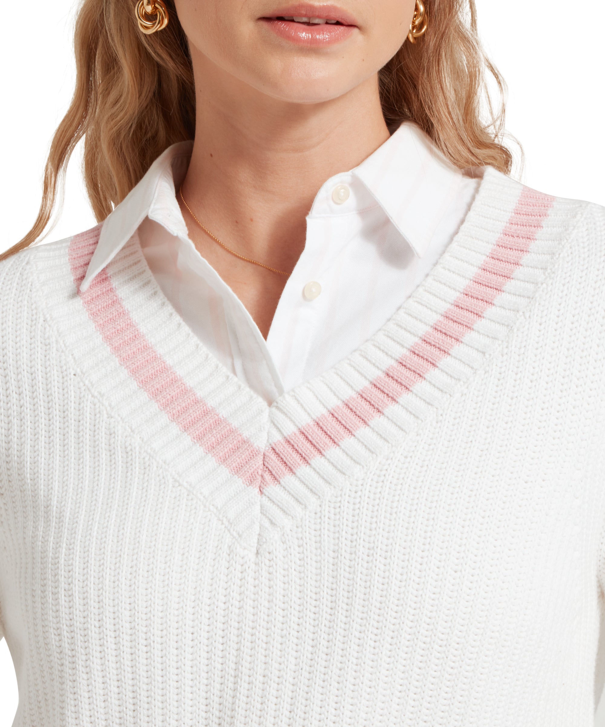 A close-up image of a female model wearing a white Schöffel jumper with pink trim on V-neck collar and cuffs, paired with a white shirt and gold accessories.