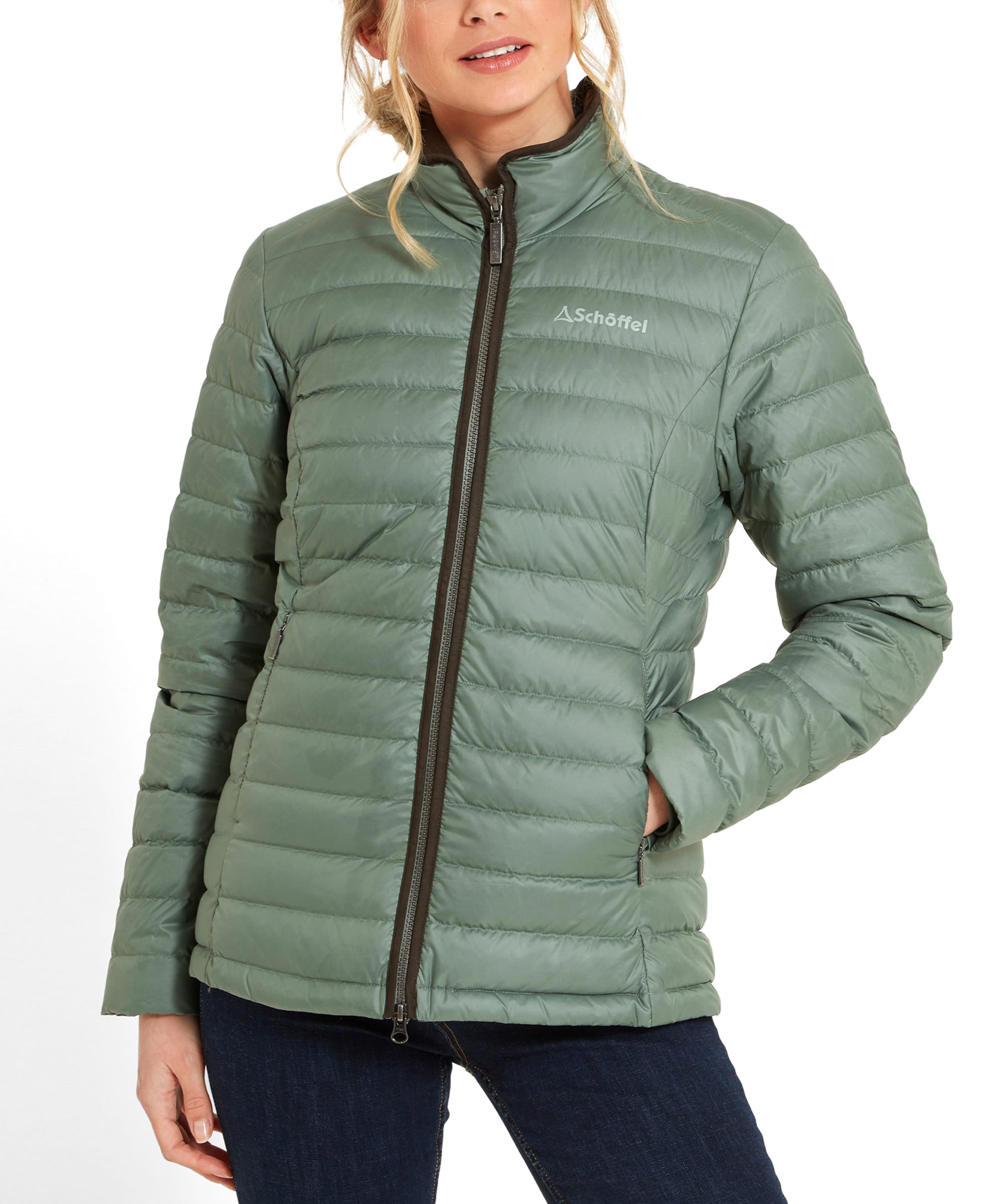 A close-up view of a woman wearing a Schöffel Hambleton Down Jacket for Women in Green, emphasising the jacket's front zip and high collar. She is smiling slightly, with her hands in the jacket's pockets.