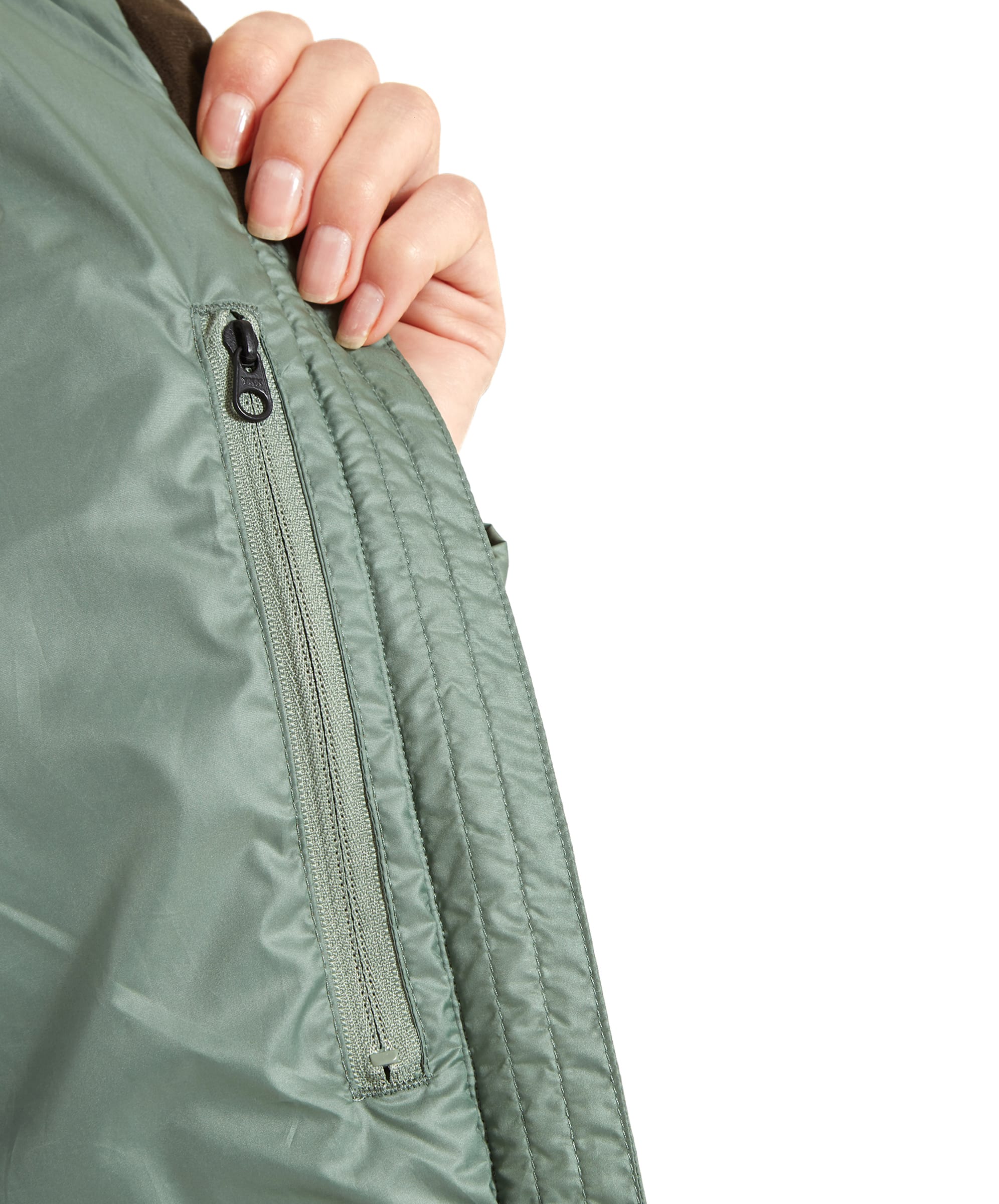 A close-up view of a woman opening an inner security pocket on a Schöffel Hambleton Down Jacket for Women in Green, revealing a small zippered compartment inside the jacket lining.