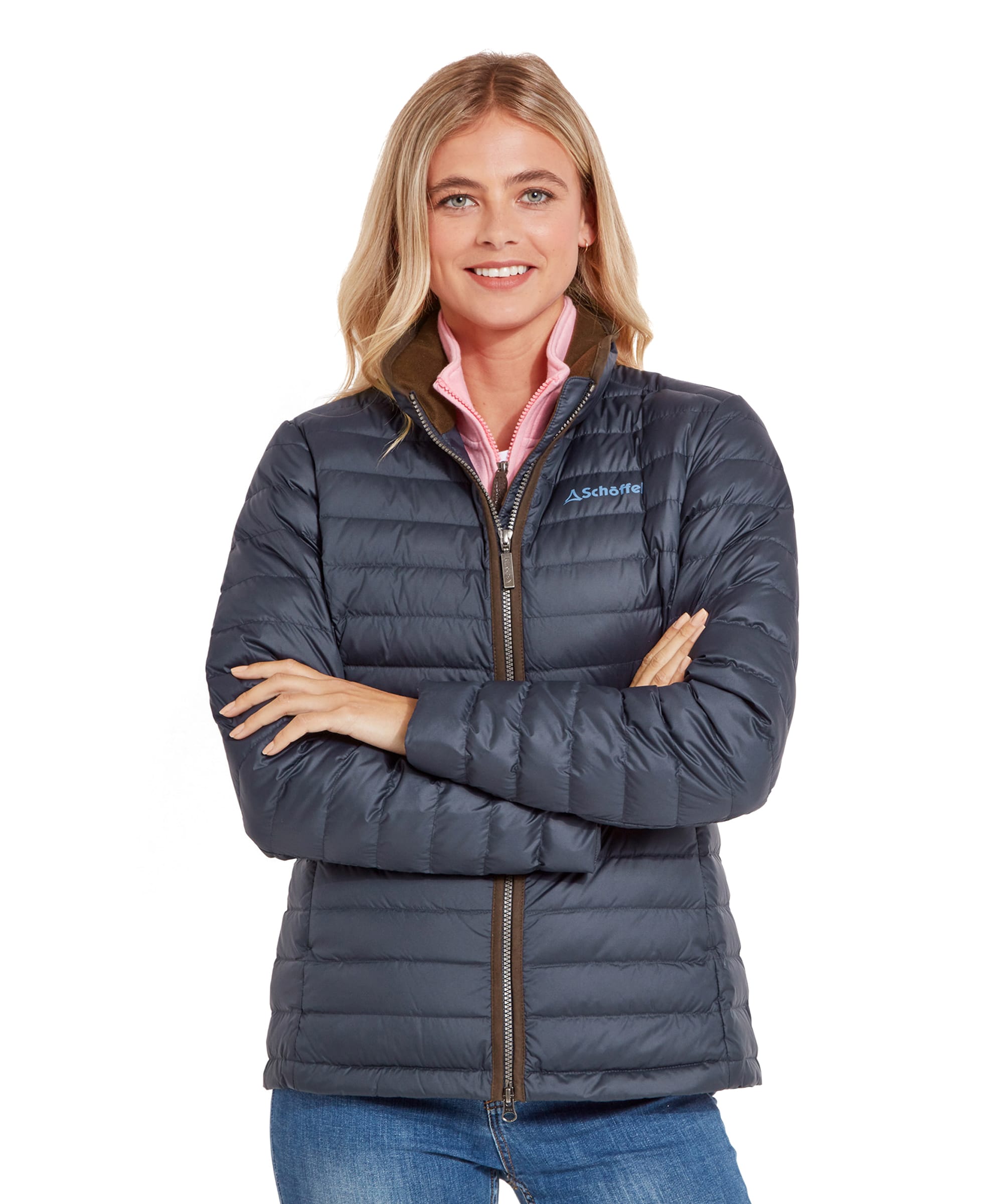 A woman smiling and wearing a Schöffel Hambleton Down Jacket for Women in Navy, with her arms crossed. The jacket is paired with a pink collared shirt underneath.