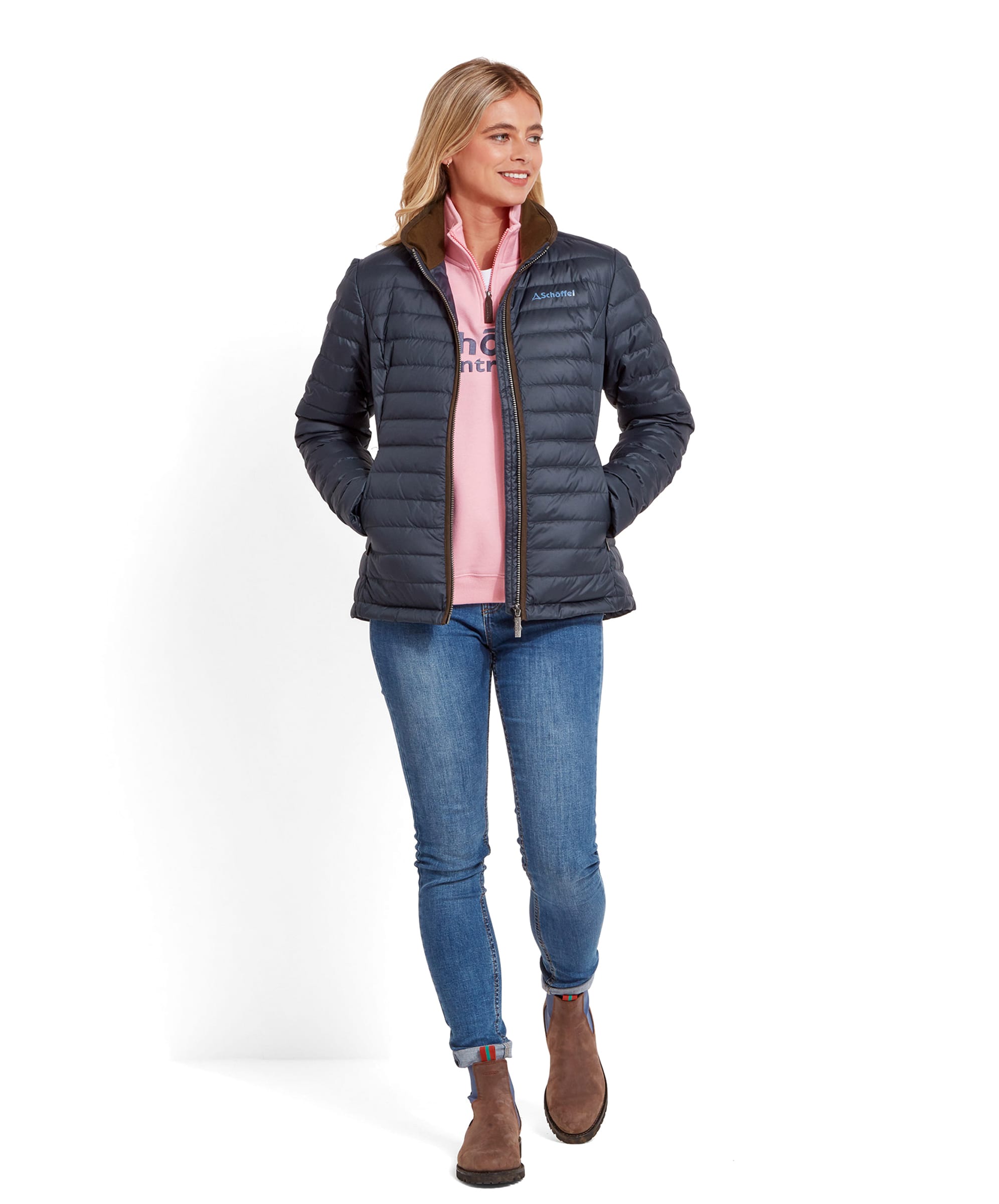 The same woman in the Schöffel Hambleton Down Jacket for Women in Navy, standing and facing forward. She is wearing blue jeans and brown boots, with a light pink sweatshirt visible underneath the jacket.