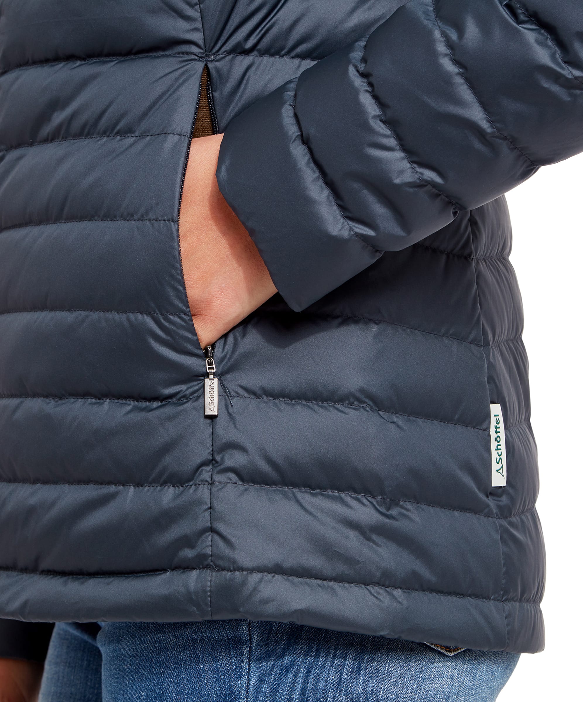 Close-up of the woman's hand in the side pocket of the Schöffel Hambleton Down Jacket for Women in Navy, focusing on the zipper and the brand tag.