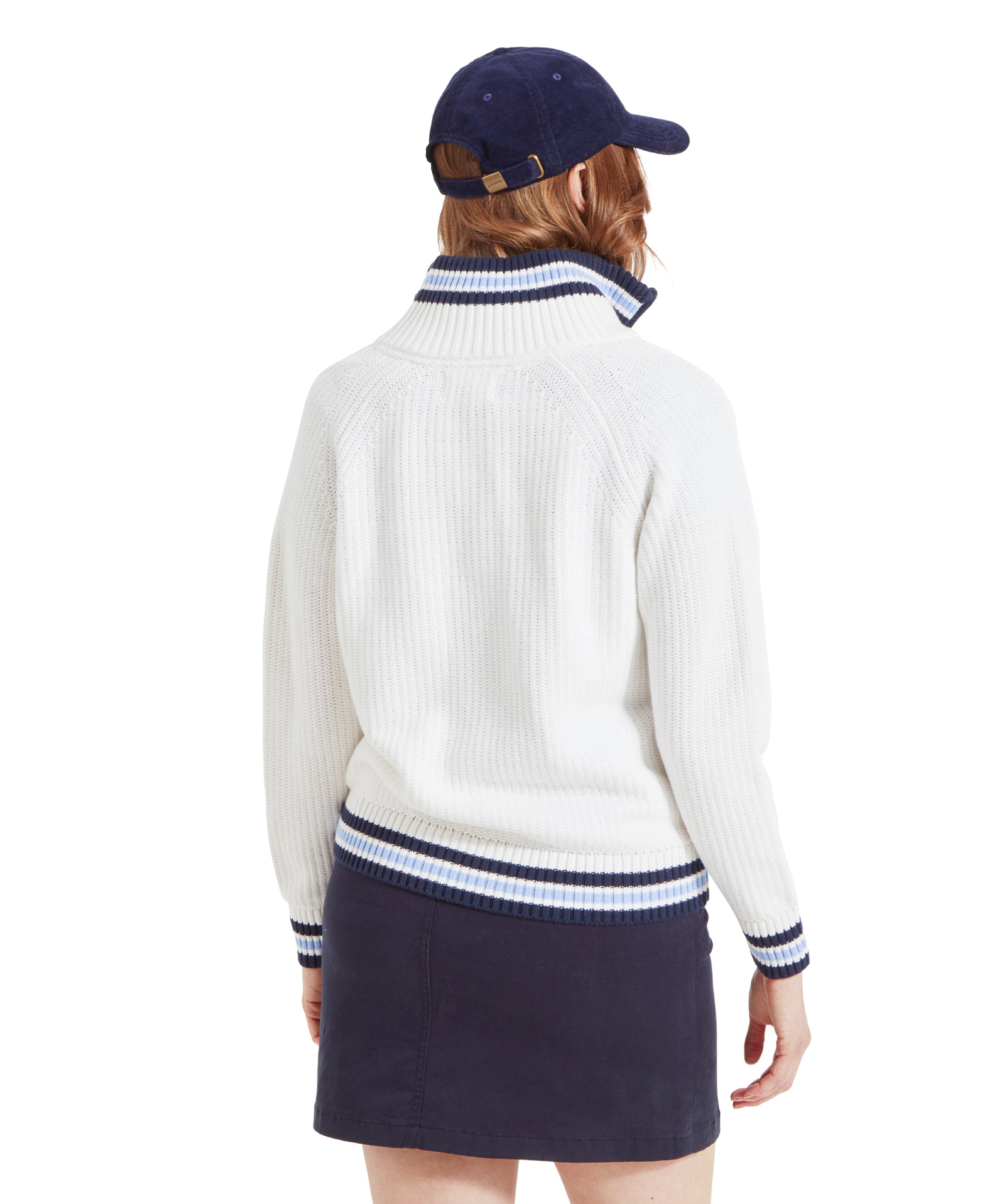 The woman is turned around, displaying the back of the white jumper with blue and white striped accents on the collar, cuffs, and hem, and a navy blue mini skirt. The back of the navy blue cap is also visible.