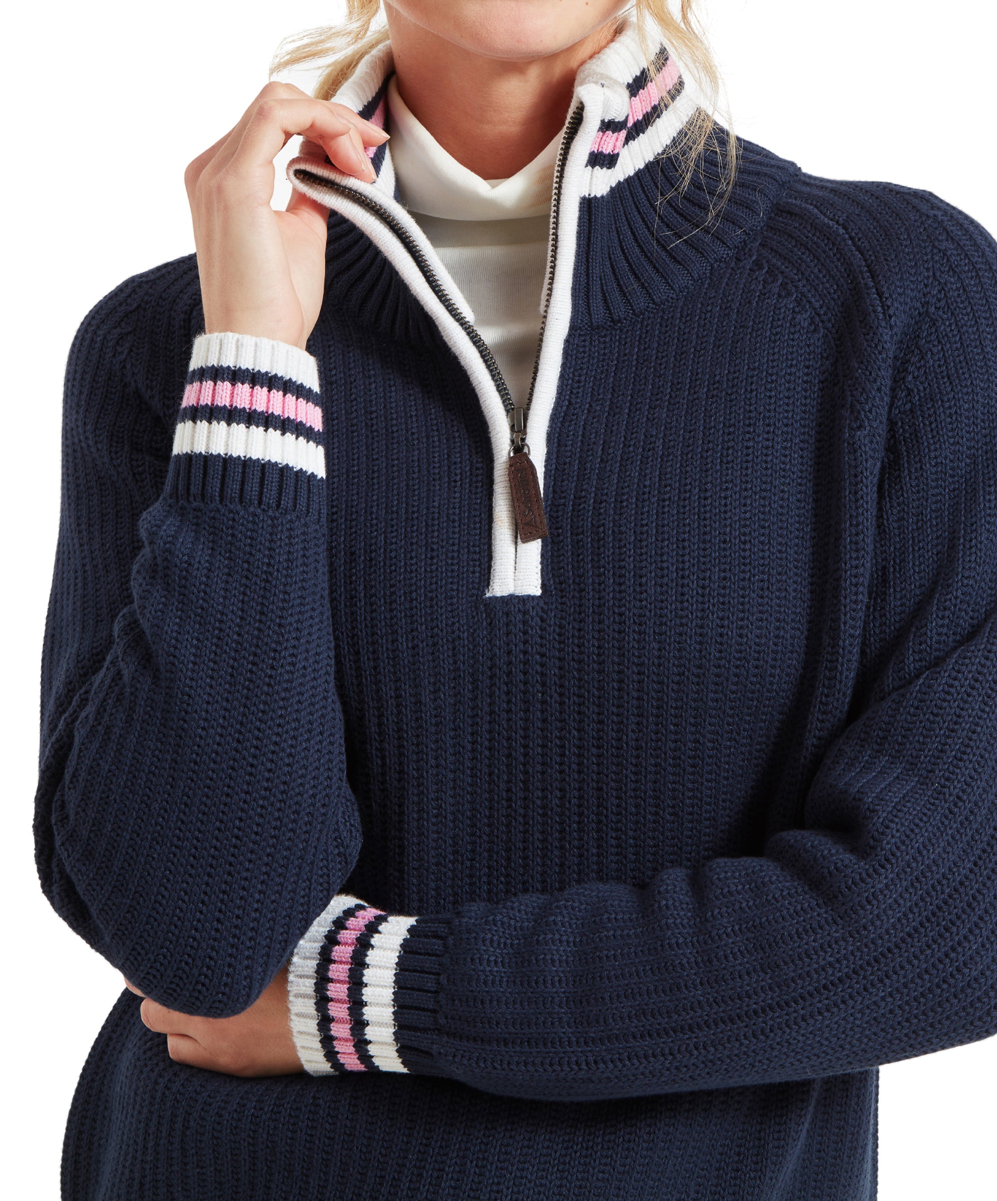 A close-up of the woman's upper body, showing her adjusting the zipper of the Schöffel Havelet Bay 1/4 Zip Jumper for Women in Navy with white, pink, and navy striped accents. She is wearing a white turtleneck underneath.