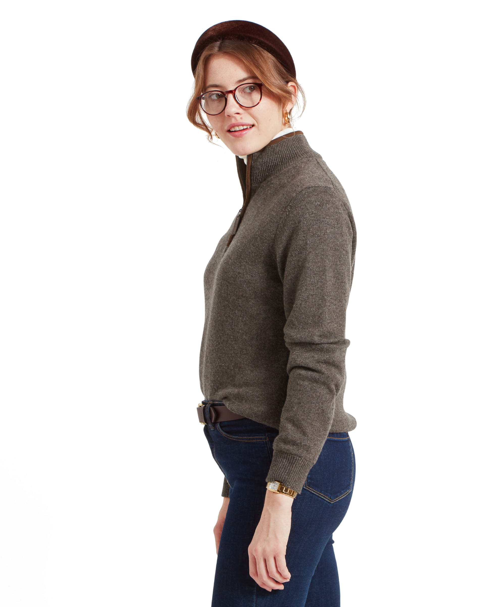 A side view of a woman standing in a Schöffel Women's Lambswool Aerobloc 1/4 Zip for Womens in Brown, dark blue jeans, and a brown headband. She is looking back over her shoulder.