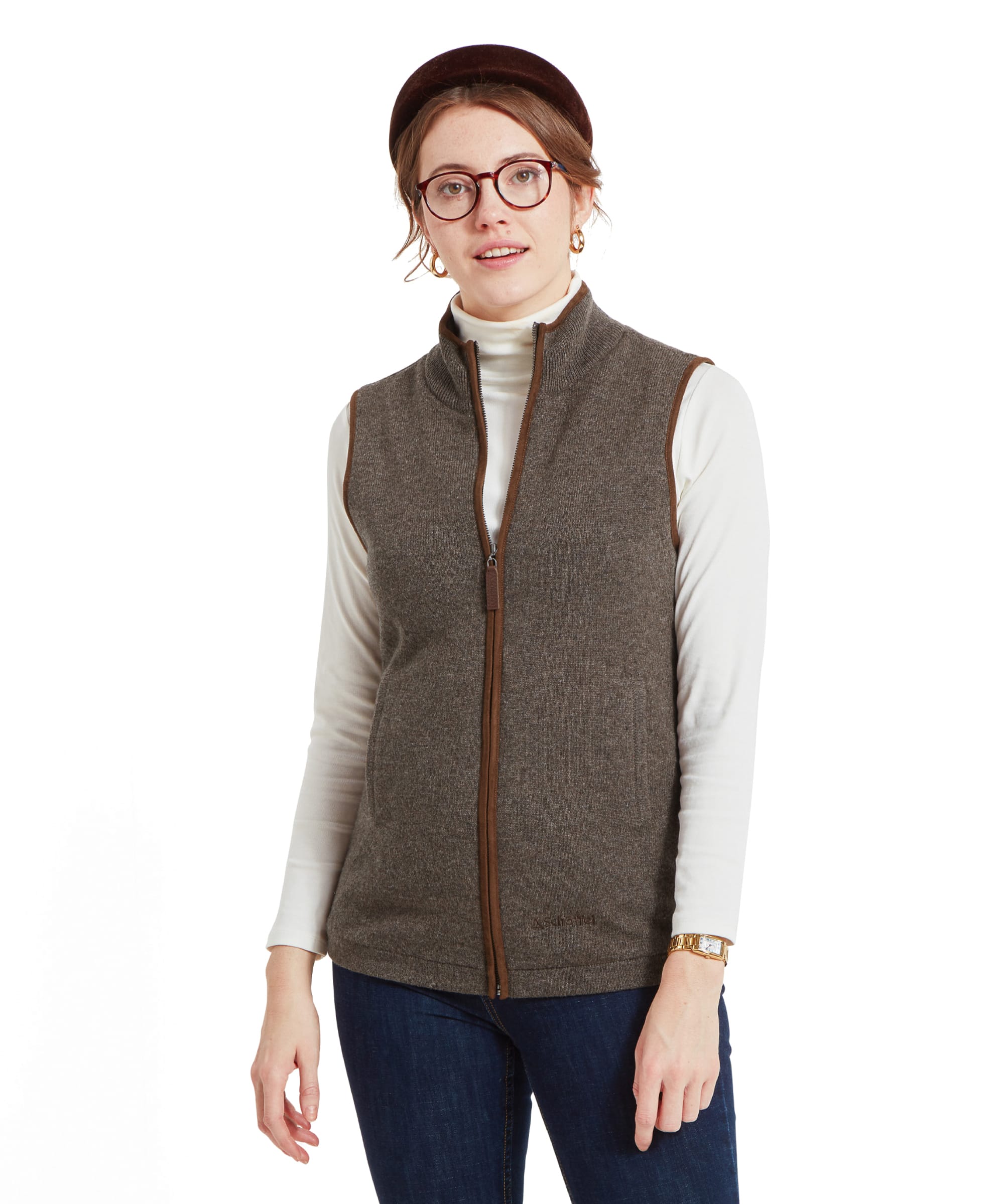 Woman wearing a Schöffel Women's Lambswool Aerobloc Gilet for Womens in Brown, standing with hands in pockets. She is also wearing a white turtleneck underneath and glasses.