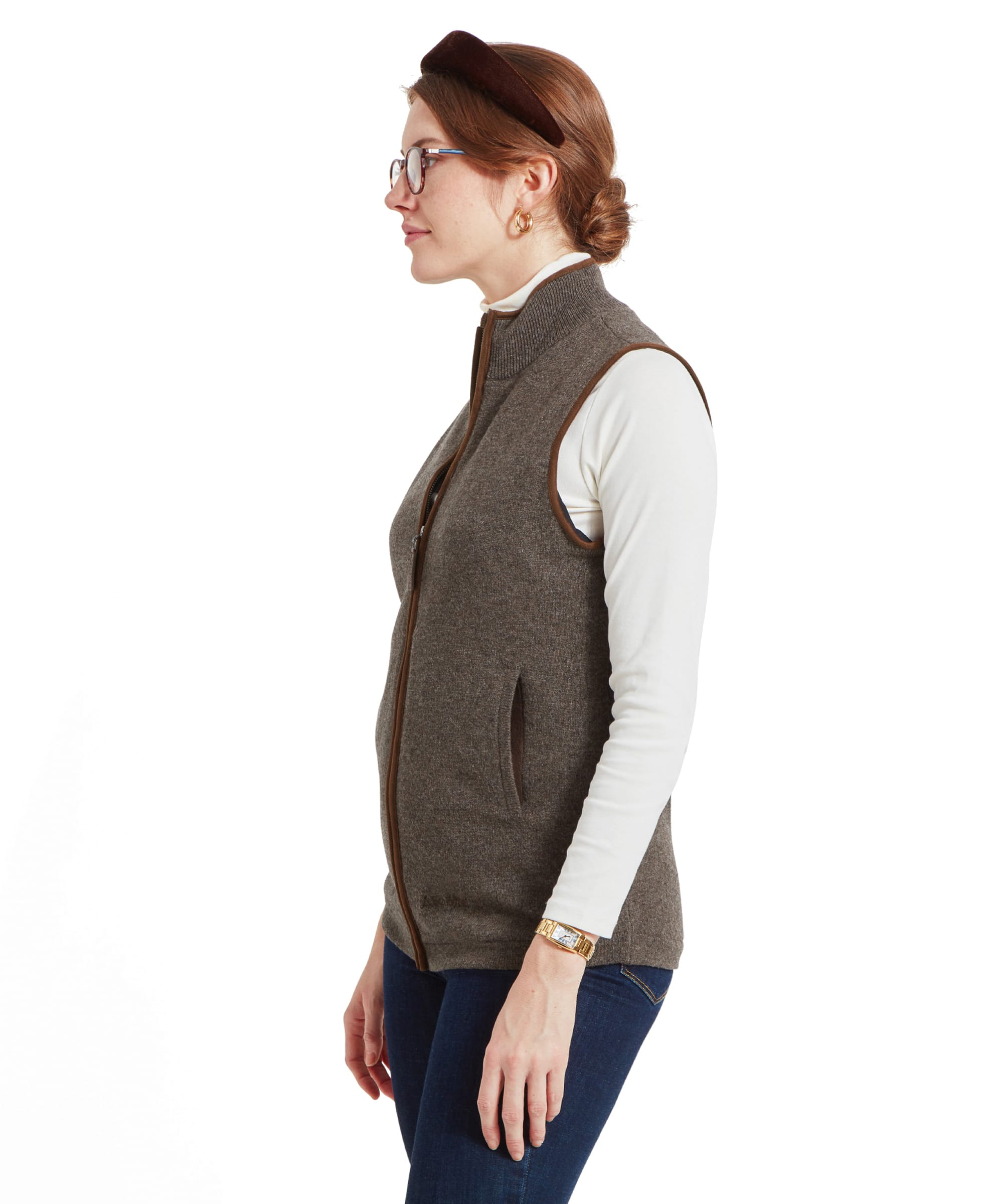 Side profile of a woman wearing a Schöffel Women's Lambswool Aerobloc Gilet for Womens in Brown. She is also wearing a white turtleneck and has her hair styled in a low bun.