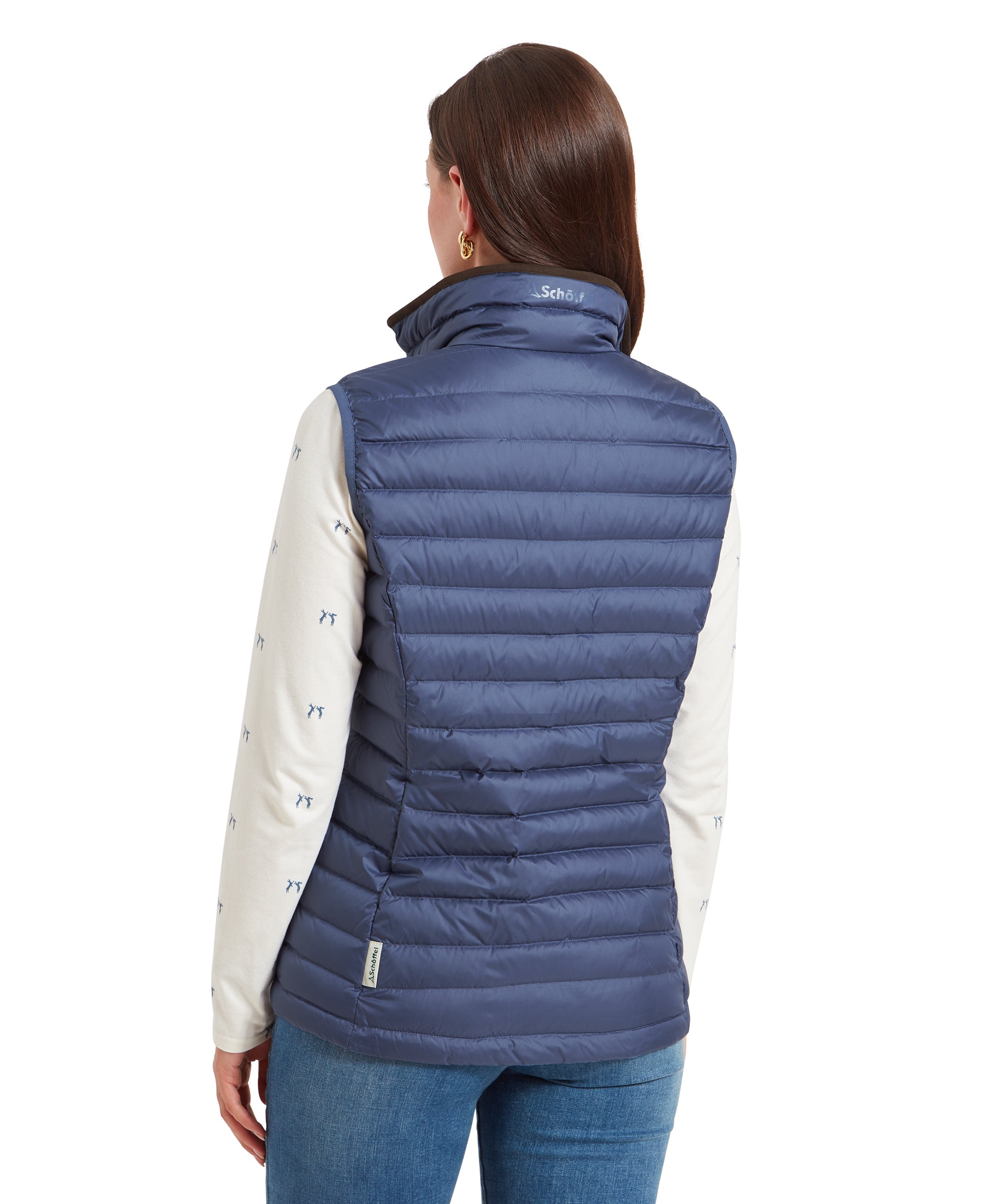 A back view of the same woman wearing the Schöffel Launde Down Gilet for Women in Blue with a cream long sleeve top with a sutble hare print detail. The gilet is complete with a "Schöffel" brand to the back of the collar and a logo pip to the seam.