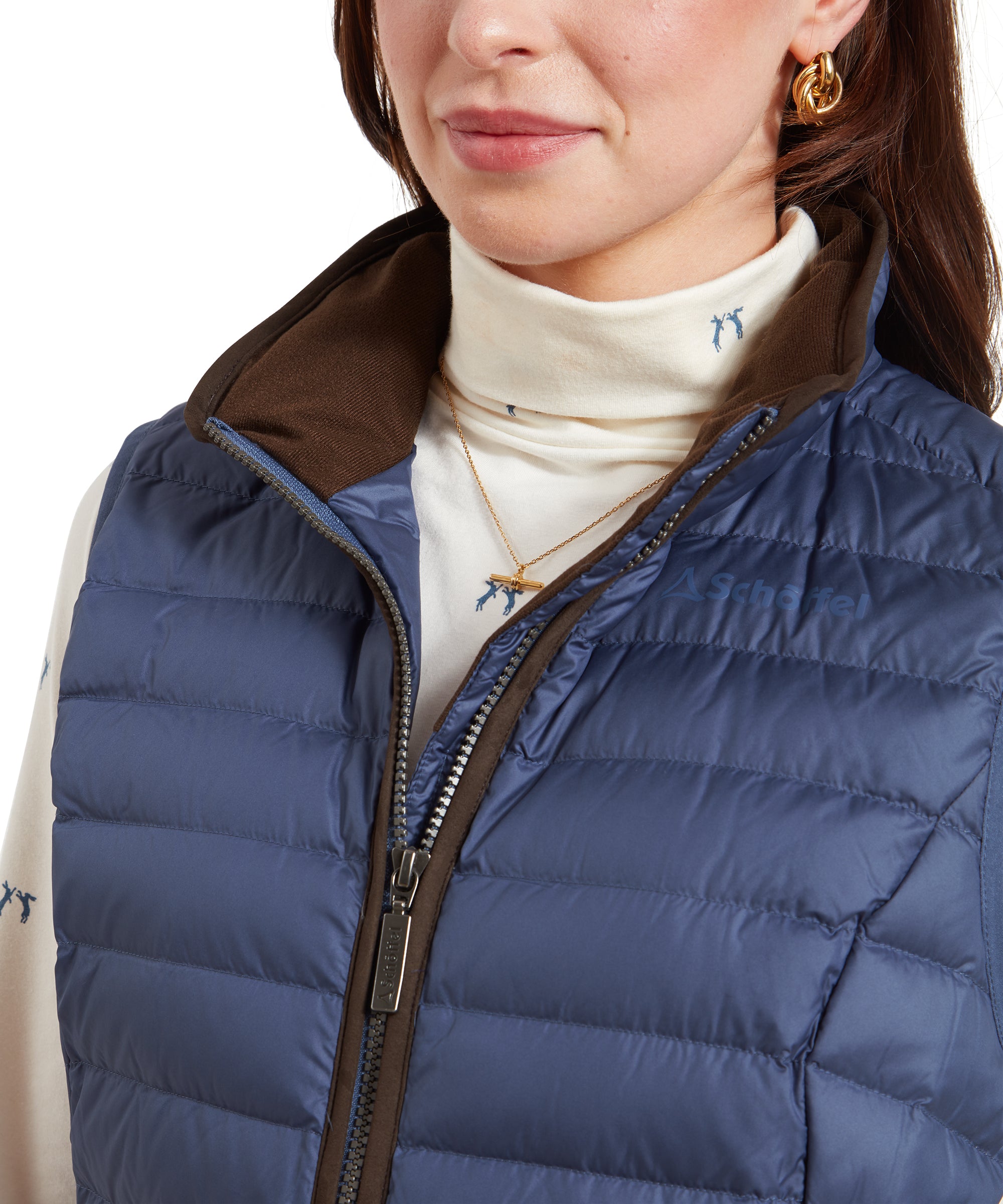 A close-up of the upper part of the Schöffel Launde Down Gilet for Women in Blue highlighting the suedette trimming and inner collar detail. The woman accessorises with a gold pendant necklace and gold hoop earrings.