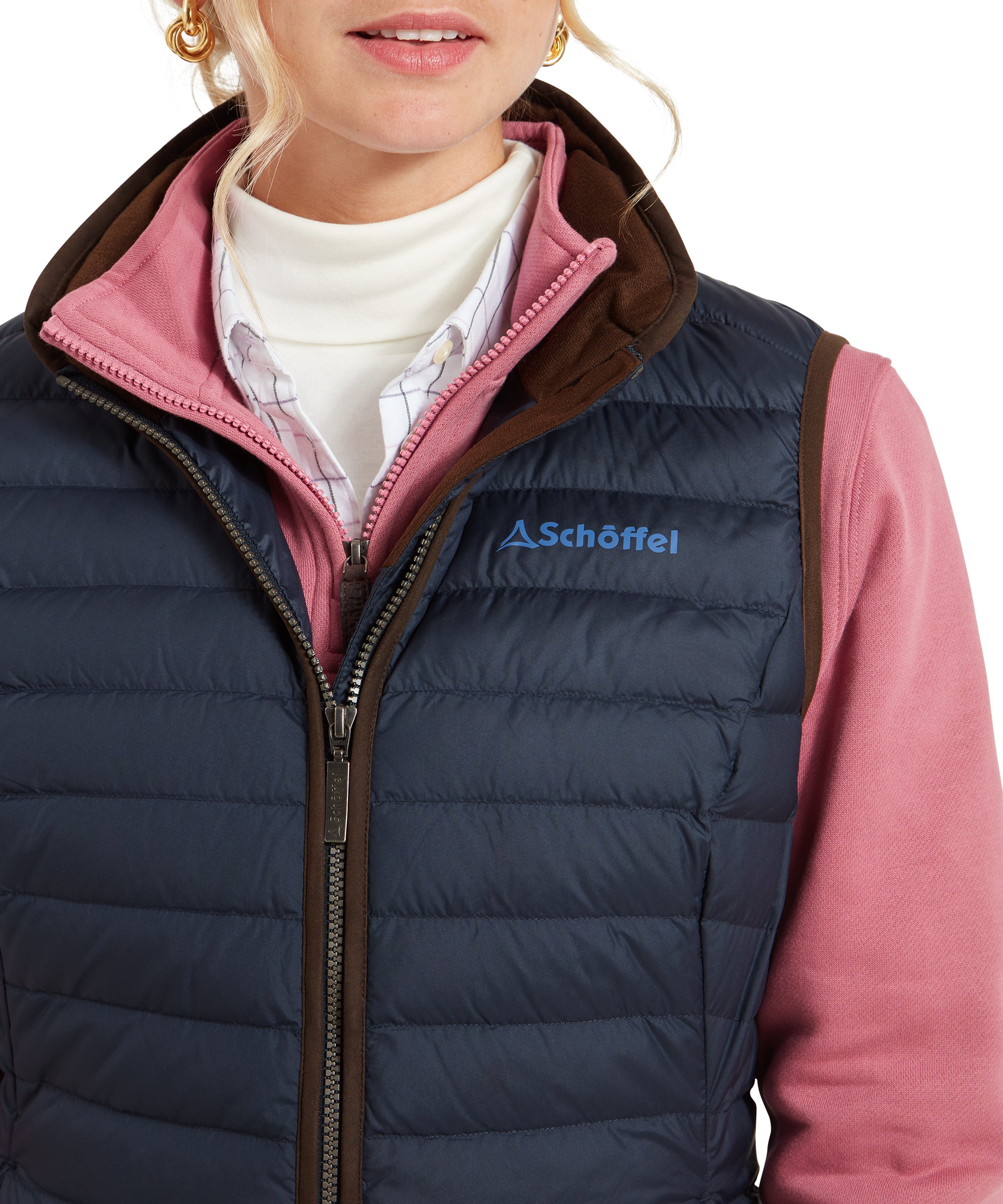 A close-up of the Schöffel Launde Down Gilet for Women in Navy’s front zipper and collar, showing the layers of clothing beneath, including a white turtleneck, a pink zip-up, and a checkered shirt.