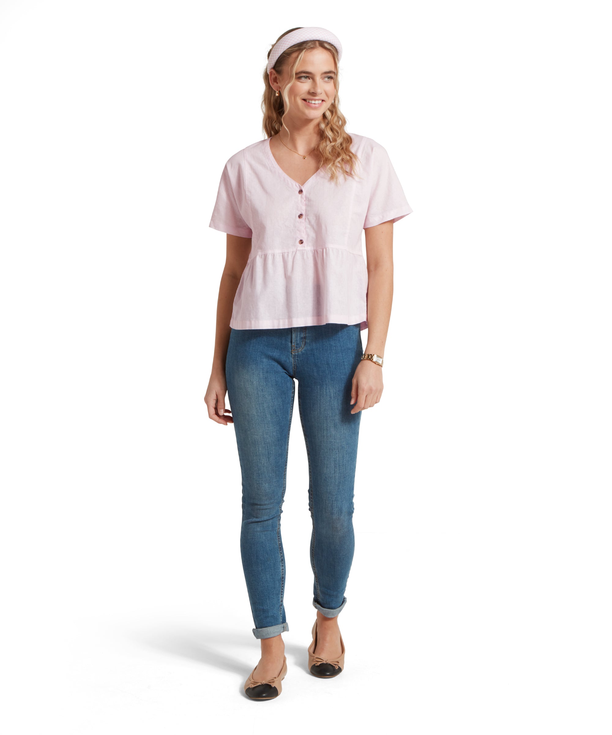 Full-height image of a female model wearing a v-neck pink linen Schöffel top, paired with mid denim jeans and tan pumps. She is standing in a relaxed pose with her hands by her side.