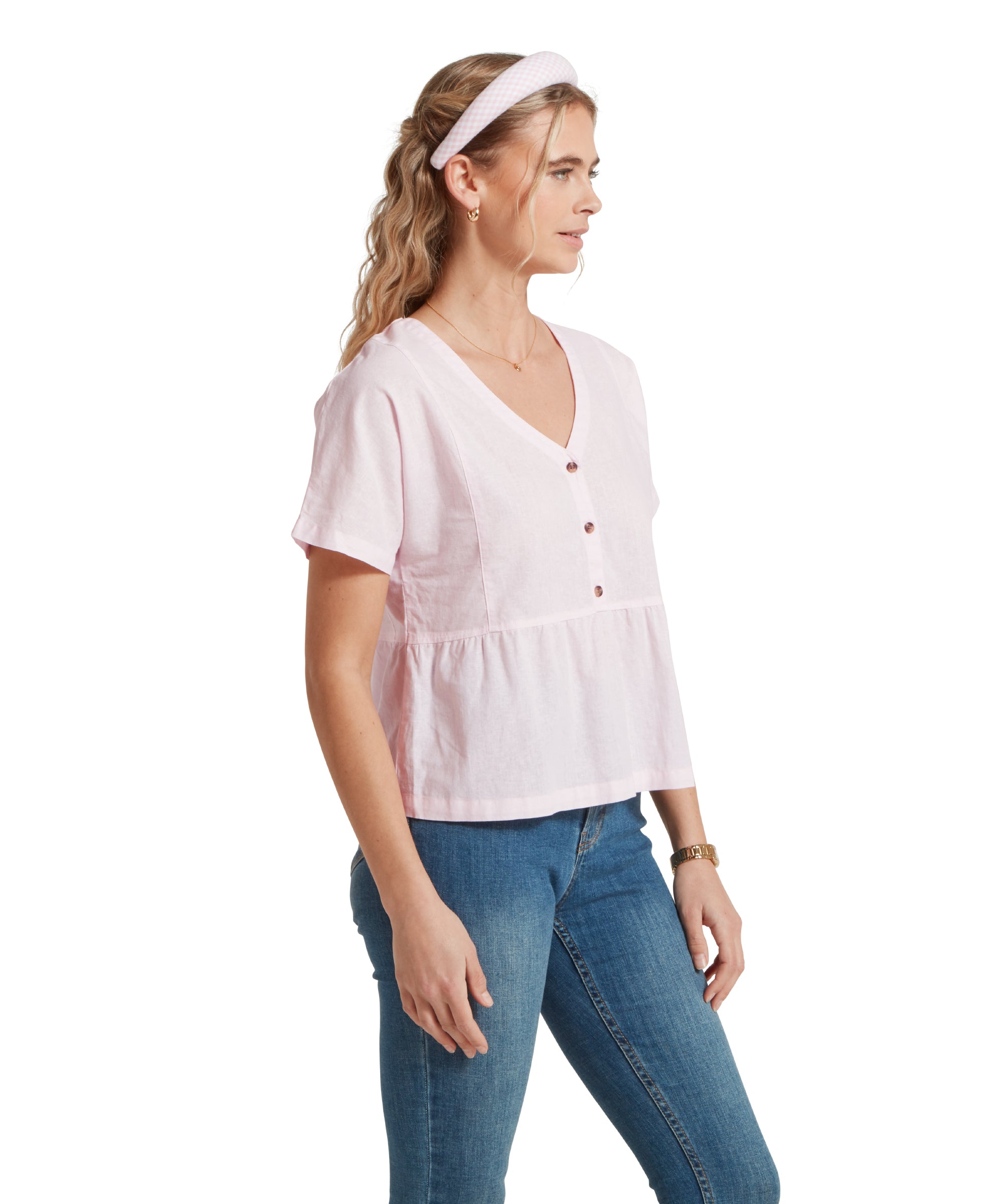 Side profile image of a female model wearing a v-neck pink linen Schöffel top, paired with mid denim jeans. She is standing in a relaxed pose with her hands by her side.