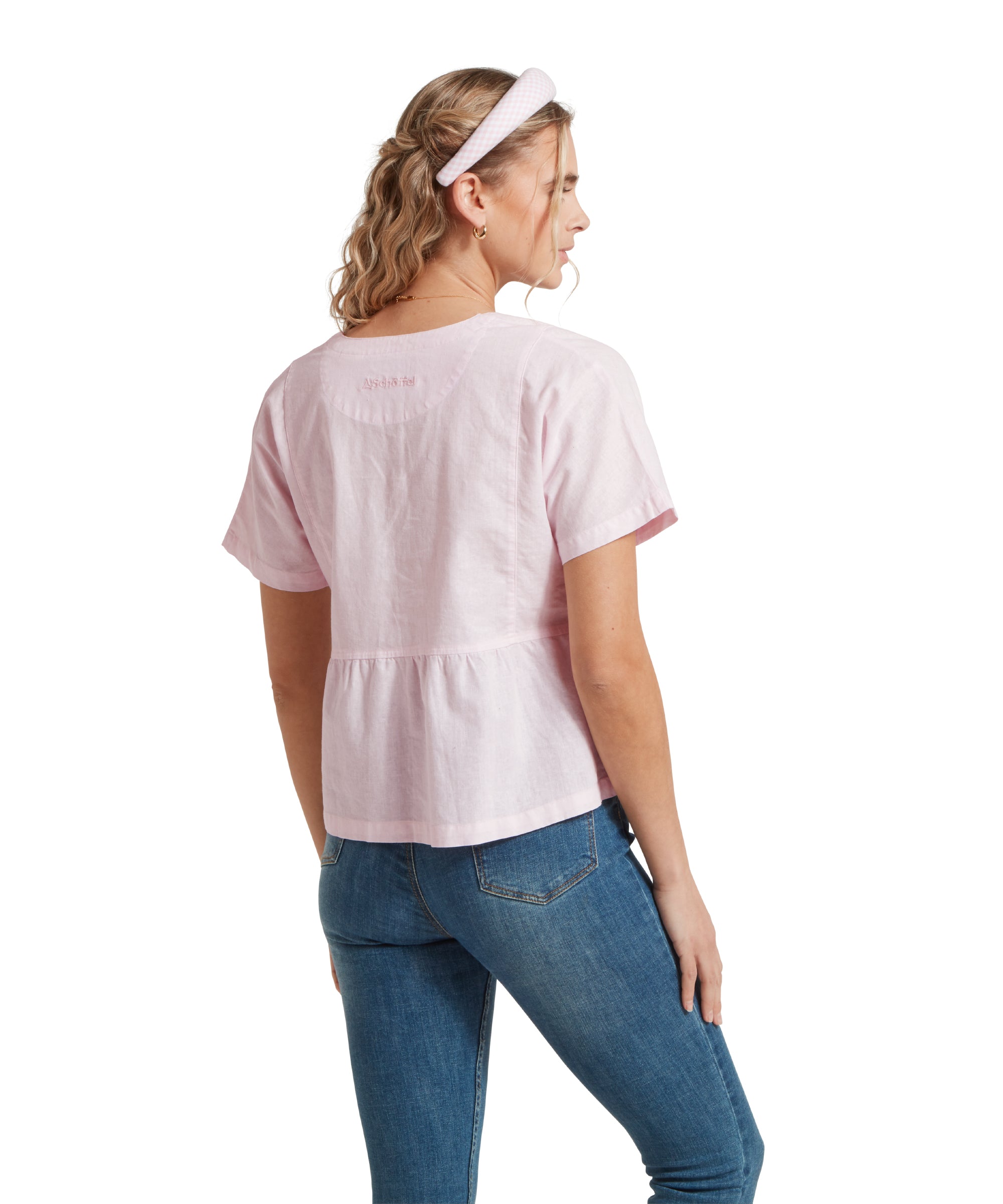 Back image of a female model wearing a v-neck pink linen Schöffel top, paired with mid denim jeans. She is standing in a relaxed pose with her hands by her side.