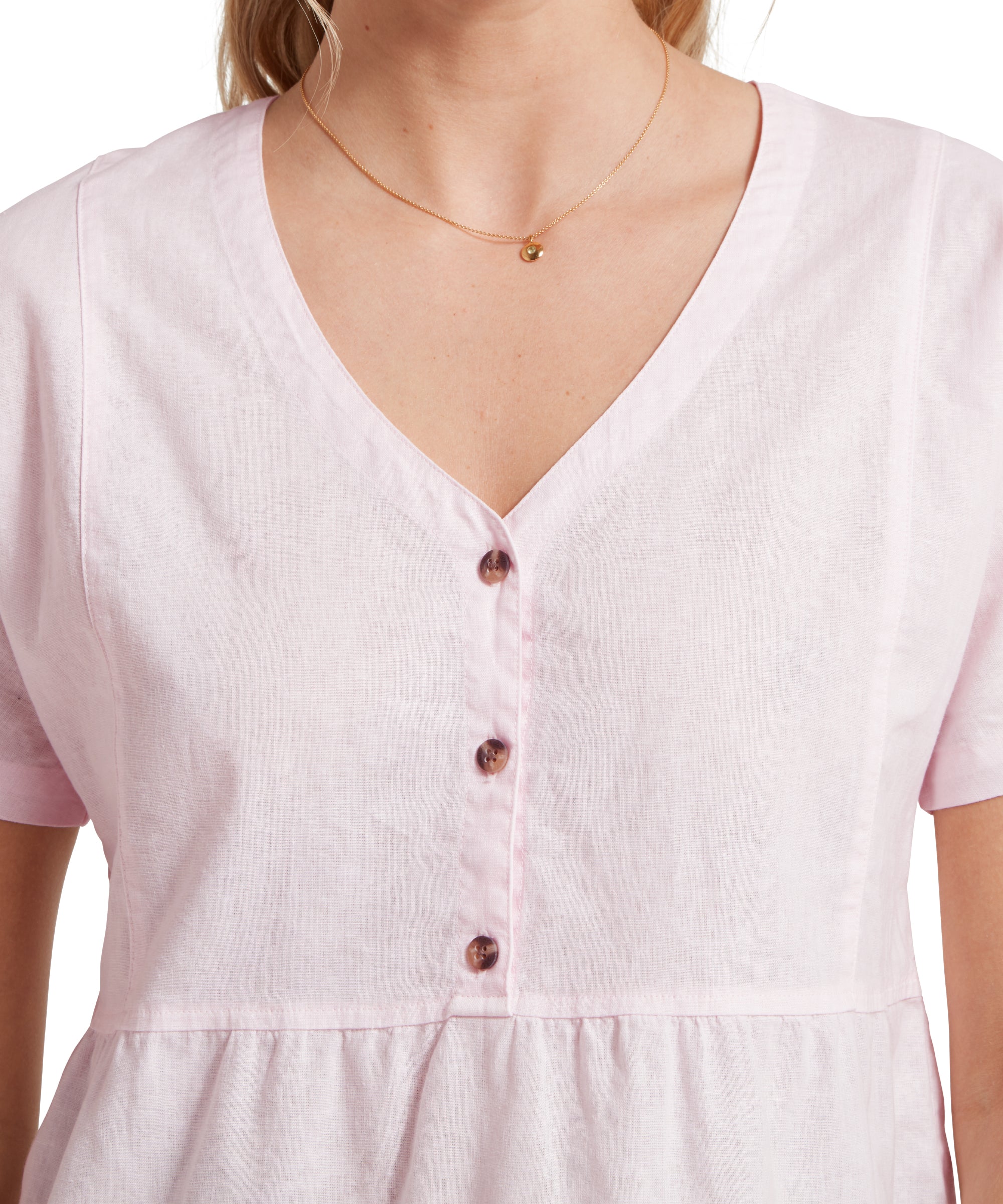 Close up image of a female model wearing a v-neck pink linen Schöffel top paired with gold accessories. Image highlights v neck and buttoned front.