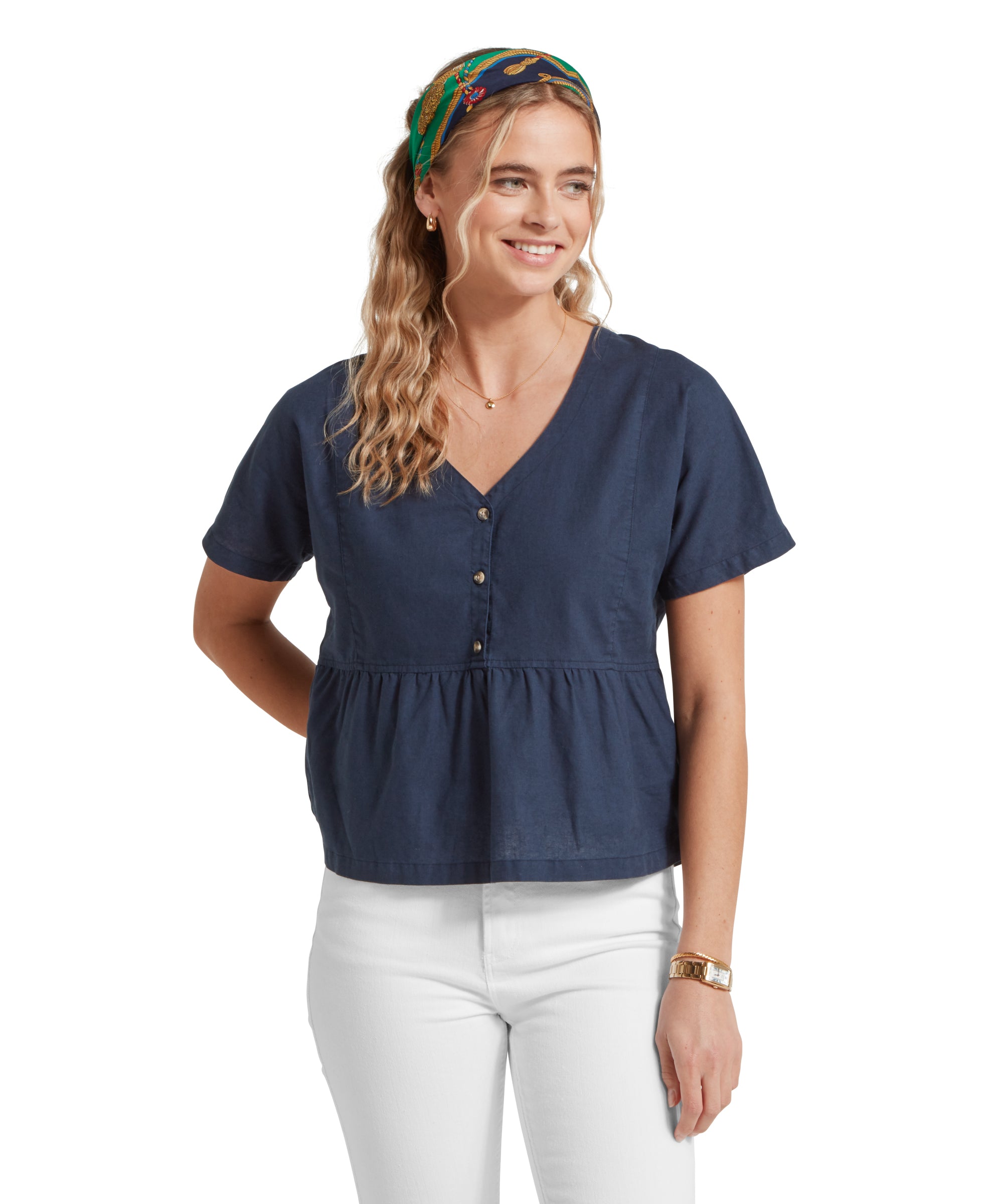 Close-up of a female model wearing a v-neck navy linen Schöffel top, paired with white jeans. She is standing in a relaxed pose with her hands by her side.