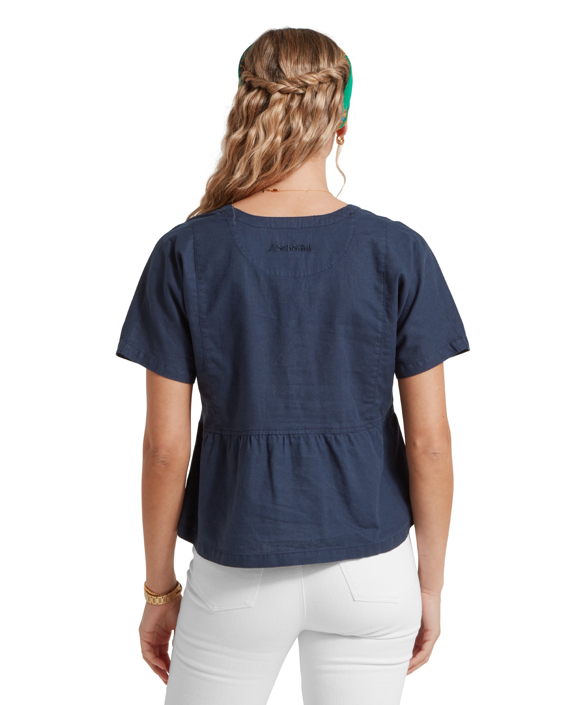 Back image of a female model wearing a v-neck navy linen Schöffel top, paired with white jeans. She is standing in a relaxed pose with her hands by her side.