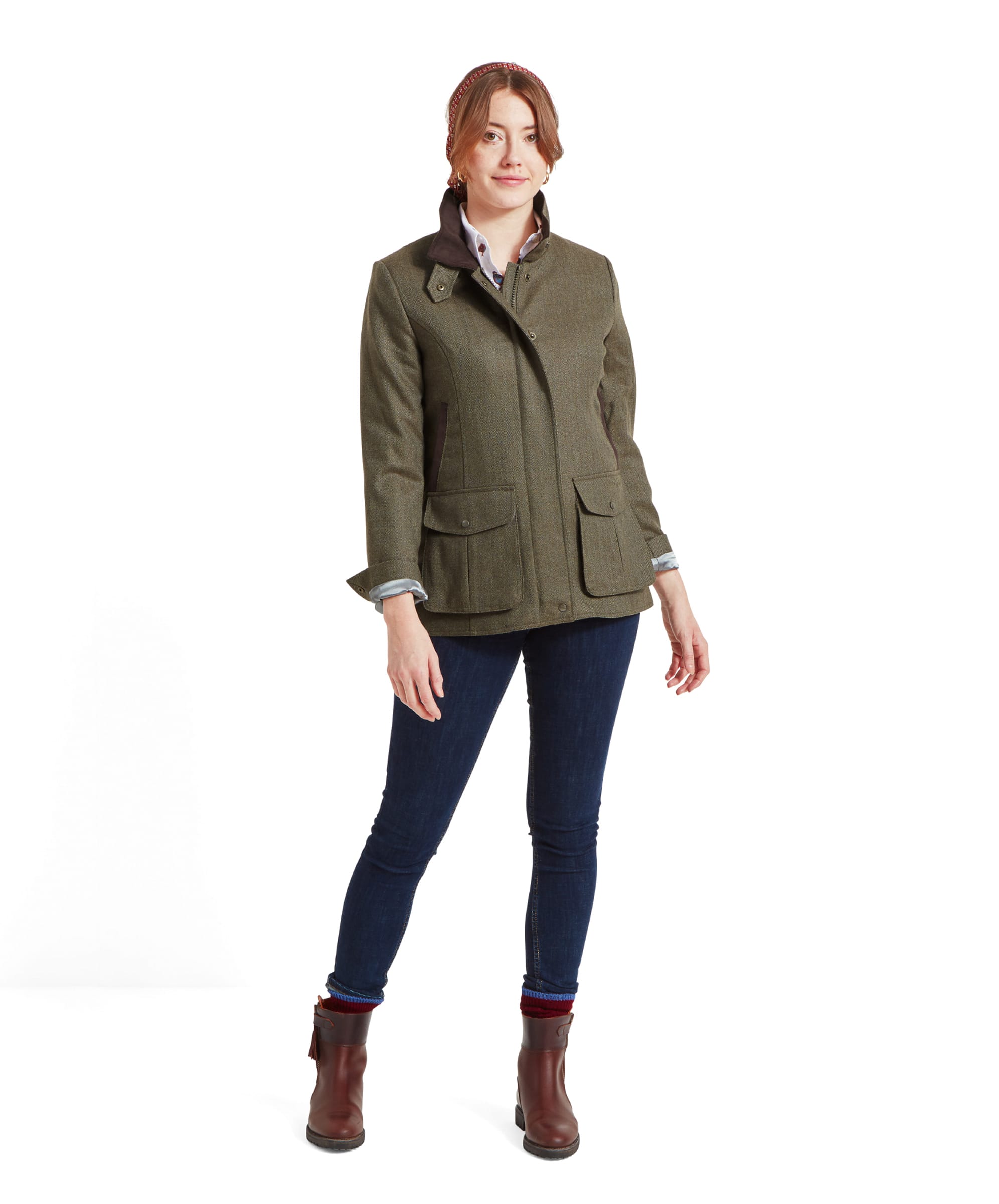 Full body view of a woman wearing the Schöffel Lilymere Jacket for Women in Green, dark jeans, and brown boots. She stands in a relaxed pose, showcasing the classic country style of the outfit.