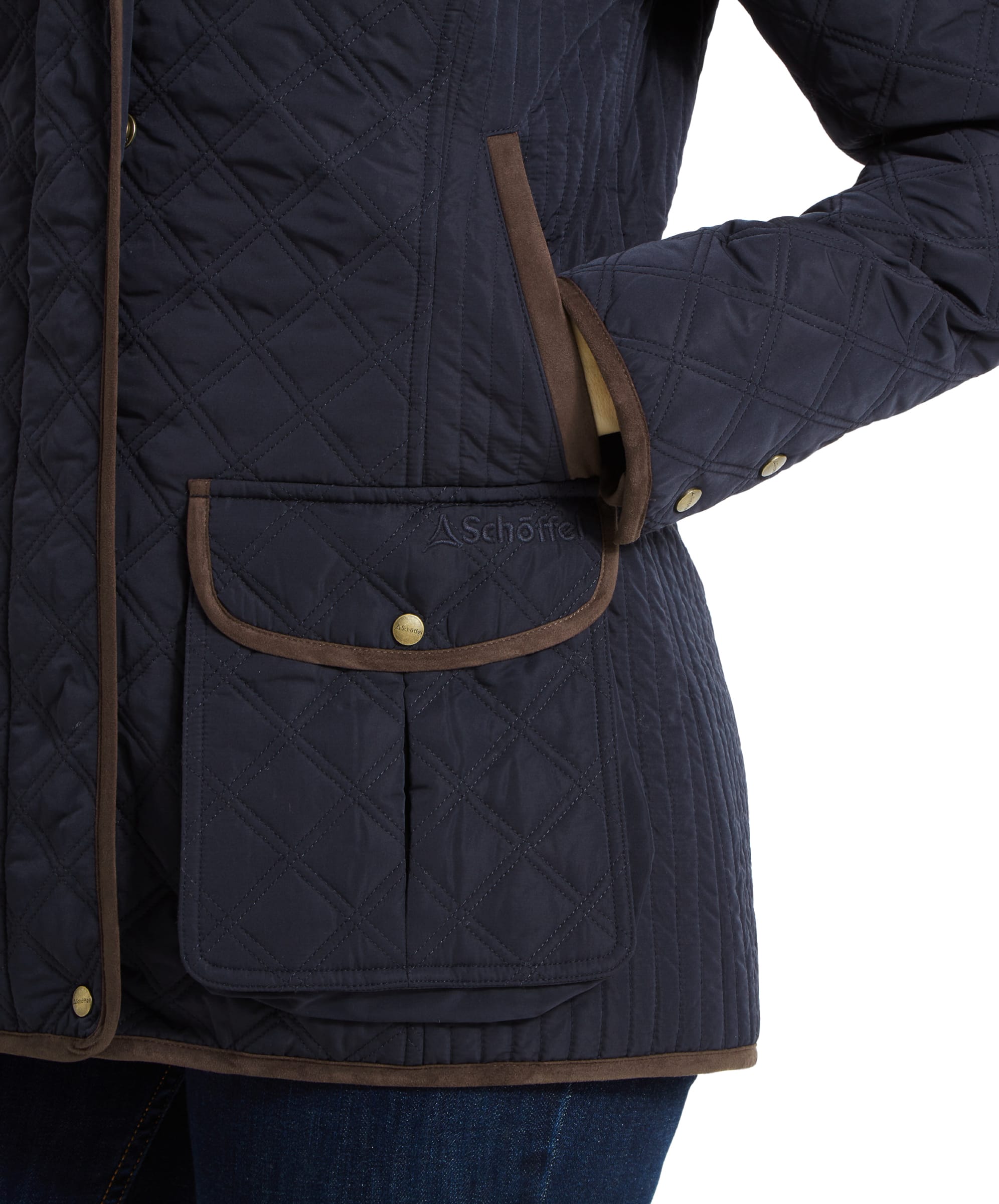 Close-up of the Schöffel Lilymere Quilted Jacket for Women in Blue's front pockets with the Schöffel logo embroidered on one of them. The brown trim highlights the diamond quilting.