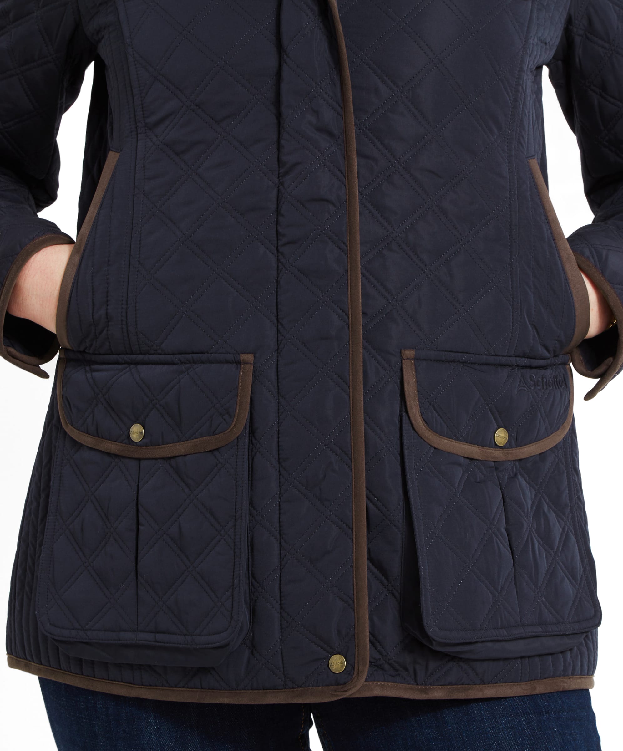 Close-up image of the lower half of a Schöffel Lilymere Quilted Jacket for Women in Blue with brown trim detailing. The focus is on the two front pockets, which have buttoned flaps and diamond quilting. The Schöffel logo is subtly embroidered on one of the pockets, and the model's hands are partially tucked into the side pockets.