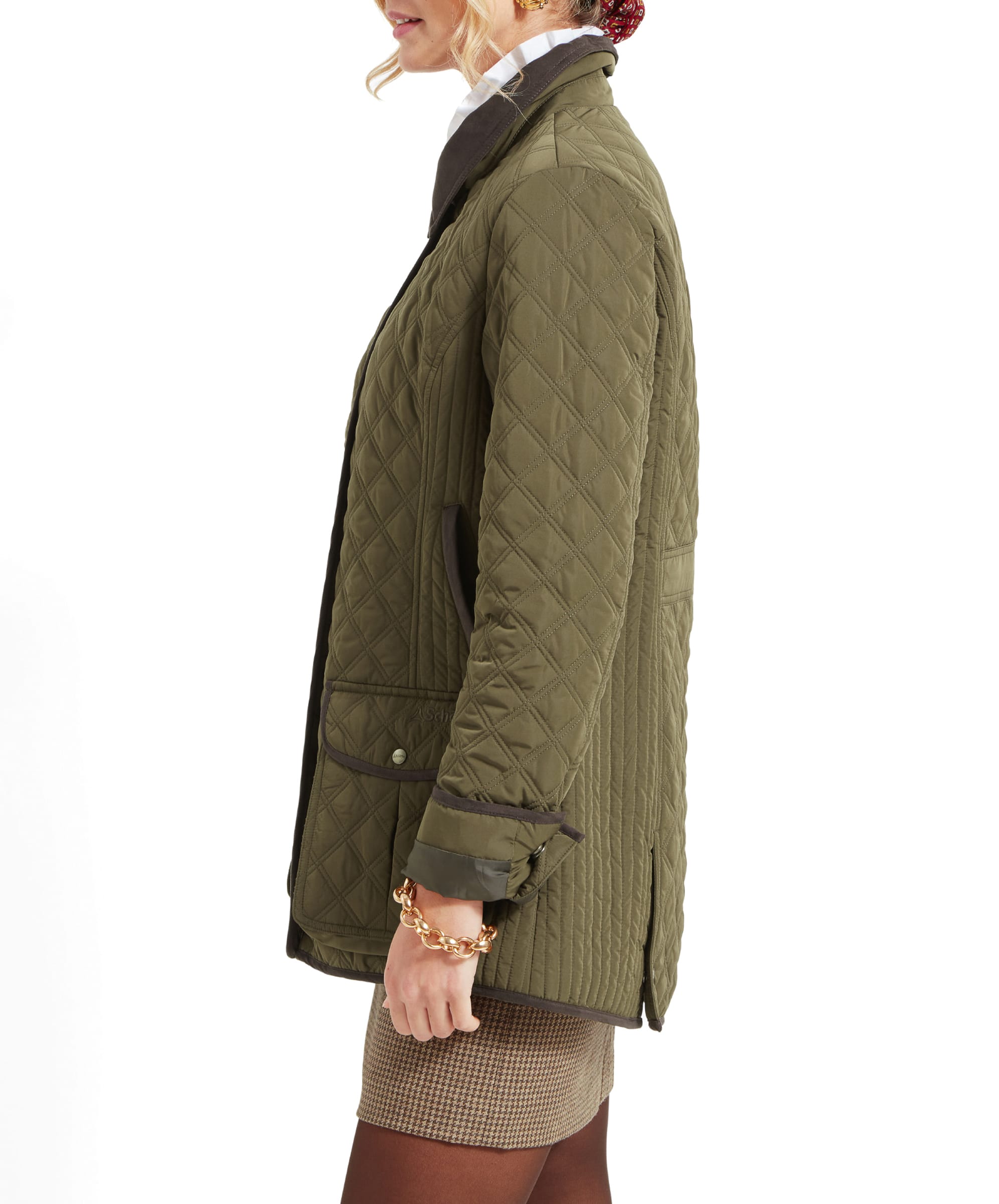 A side profile of the woman wearing the Schöffel Lilymere Quilted Jacket for Women in Green. The jacket shows a fitted waist, with brown trim details along the pocket and sleeves. The woman is looking forward with a subtle smile.