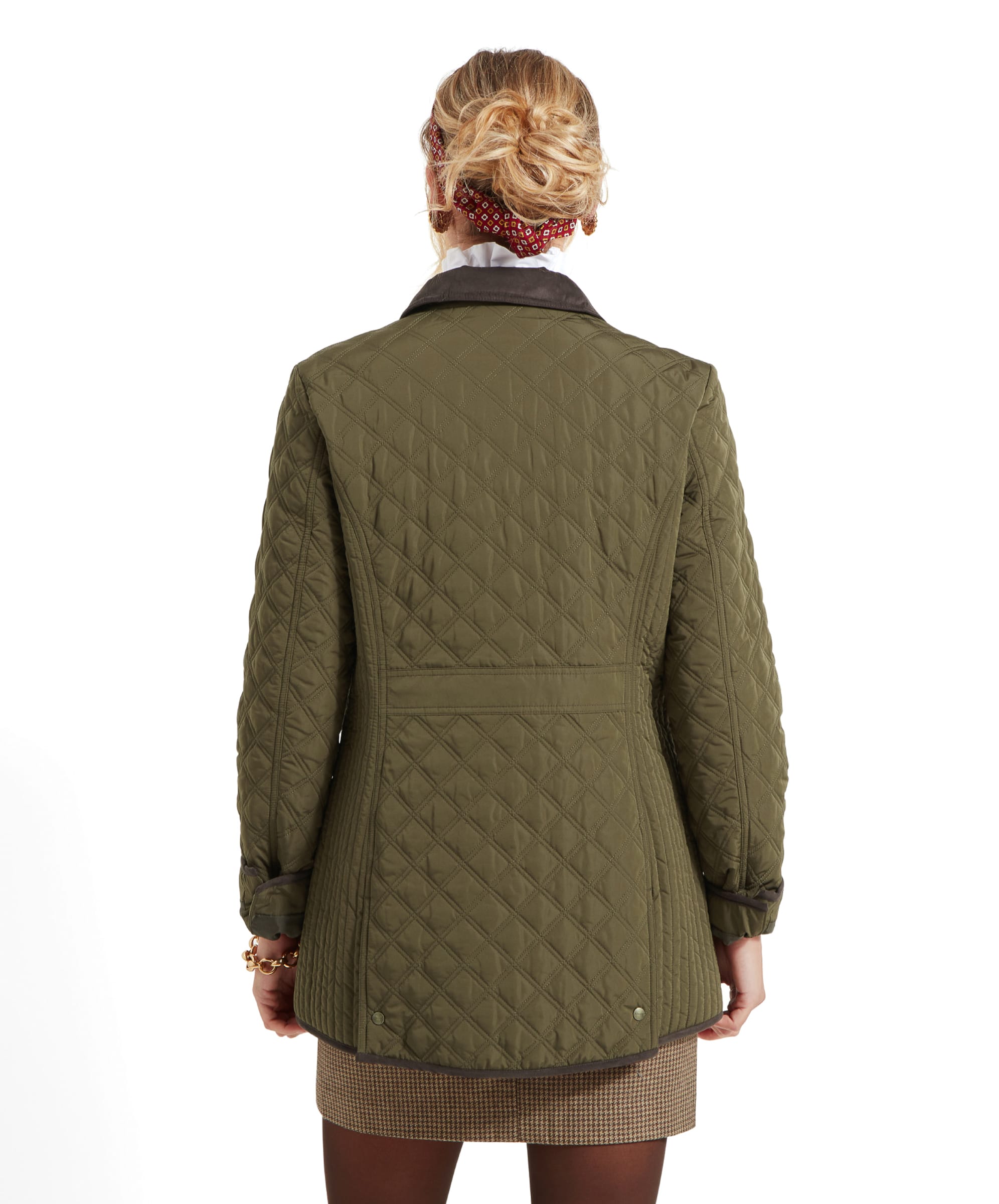 A back view of the Schöffel Lilymere Quilted Jacket for Women in Green worn by the woman. The jacket features a fitted silhouette and brown trim details. The woman’s hair is styled in a low bun adorned with a red patterned headband.