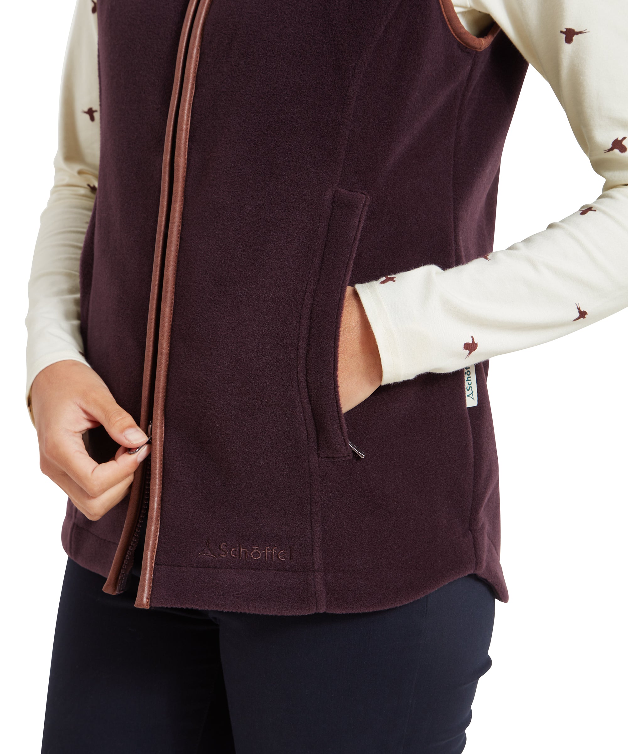 A close-up view focusing on the front of the Schöffel Lyndon Fleece Gilet for Women in Brown, showing the zip and the Schöffel logo near the hem. The zip is slightly open, revealing part of the cream top underneath.