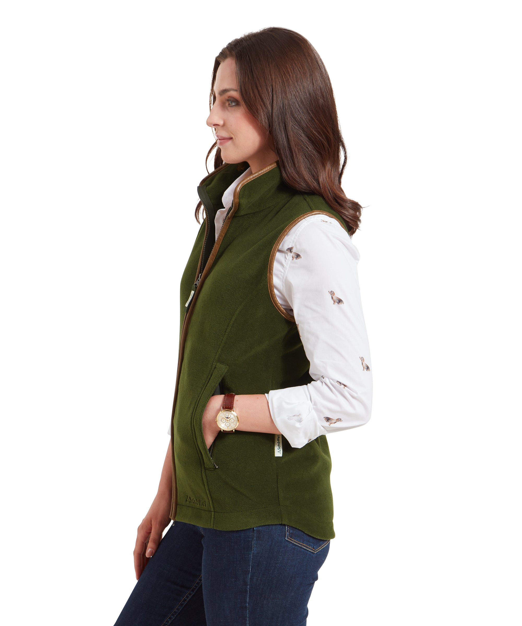 Side profile view of the woman wearing the Schöffel Lyndon Fleece Gilet for Women in Olive Green. She is looking slightly off to the side with her hands in the gilet’s pockets, showing the gilet’s fitted cut and brown trim.