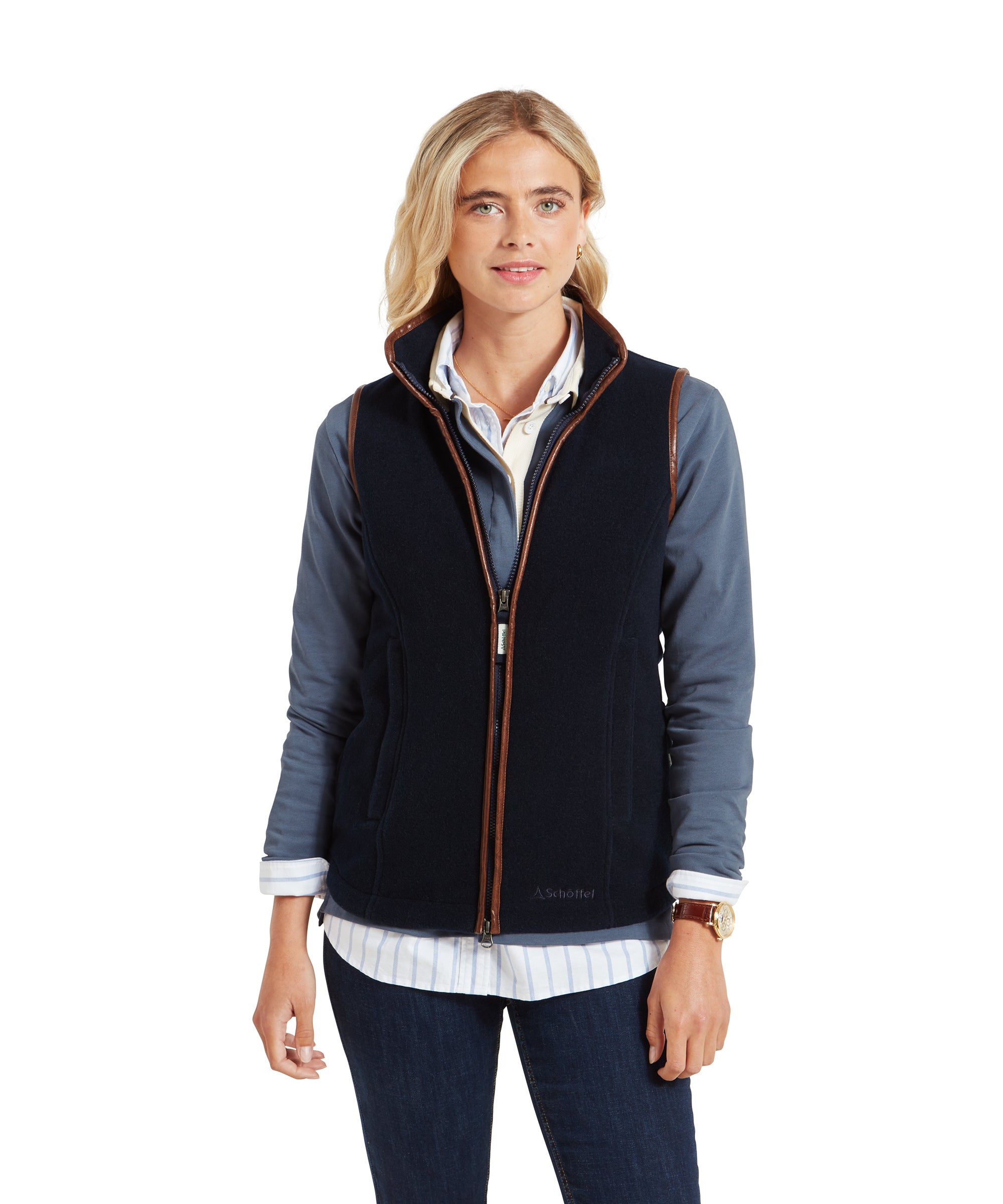 A woman is wearing a Schöffel Lyndon Fleece Gilet for Women in Navy over a light blue button-up shirt. The gilet features a full front zipper with brown trim and two side pockets. She is looking slightly to the side and smiling.