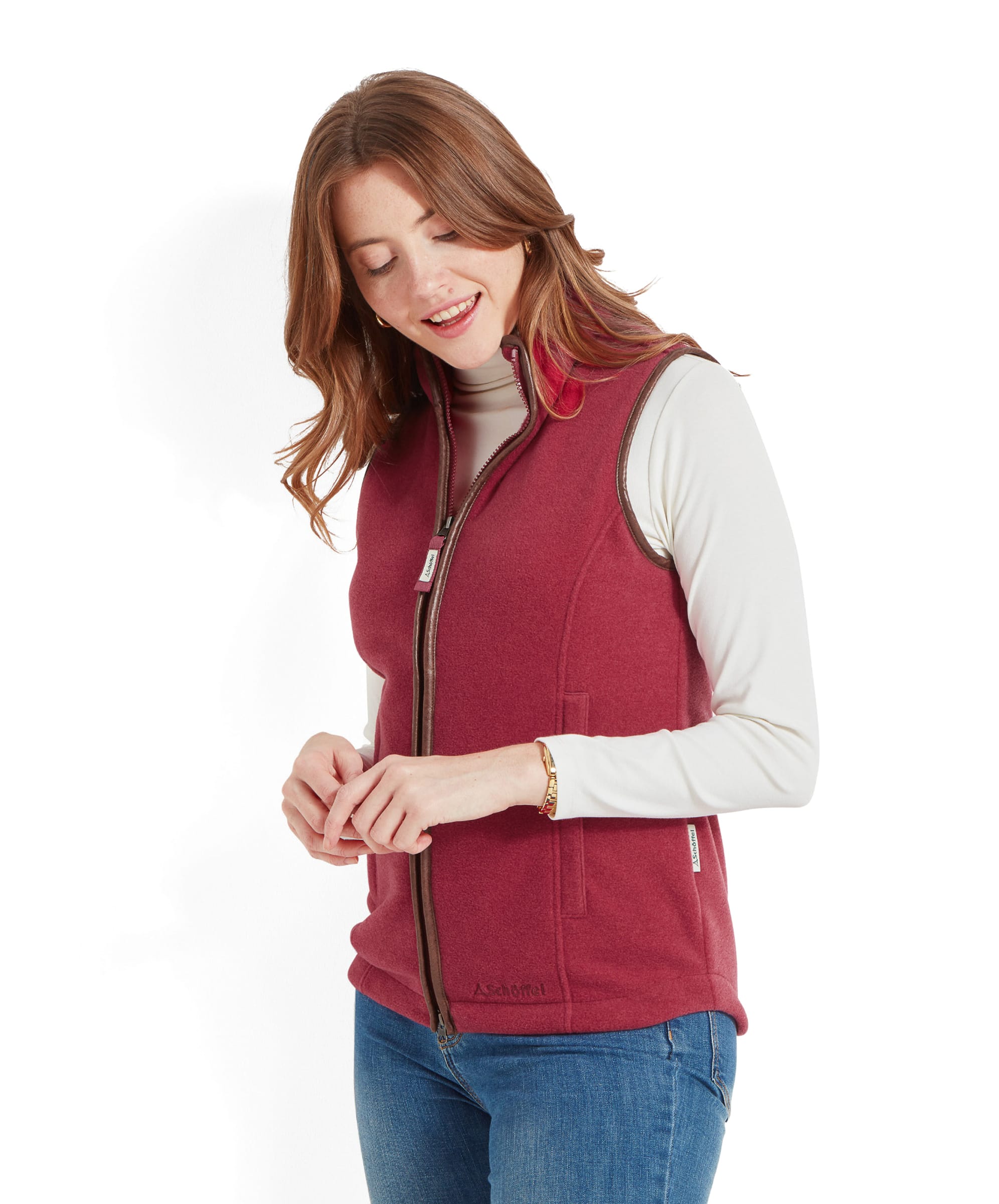 A woman wearing the Schöffel Lyndon Fleece Gilet for Women in Red, shown from a slightly angled side view. She is smiling and holding her hands together.