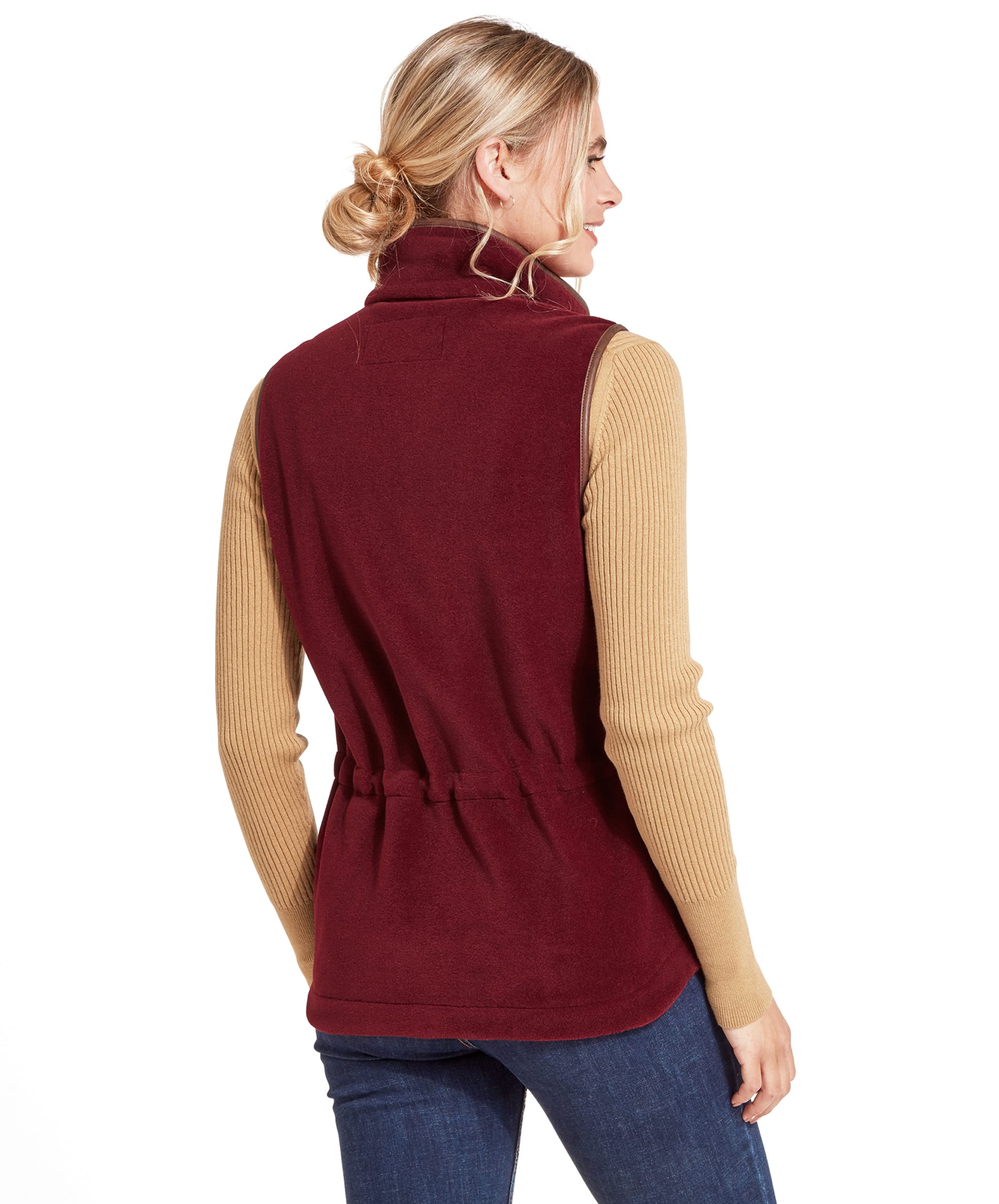 A rear view of the woman wearing the Schöffel Lyndon Fleece Gilet for Women in Deep Red, showing the fitted waist detail. She is still wearing the beige turtleneck sweater and has her hair tied back in a loose bun.