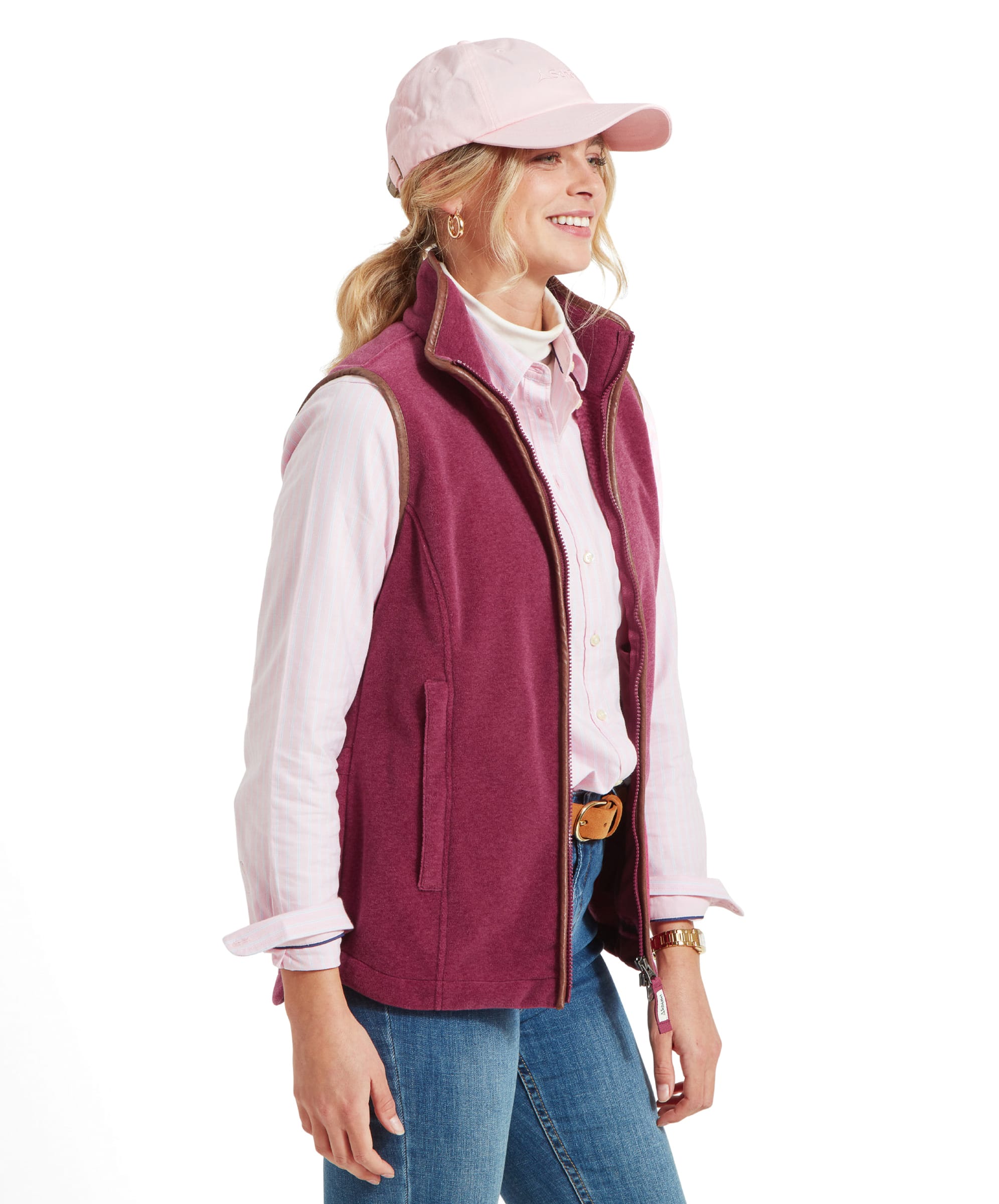 A side profile of the woman wearing the same Schöffel Lyndon Fleece Gilet for Women in Red and pale pink shirt. The gilet has a brown leather trim, and she is smiling slightly while looking to her left.