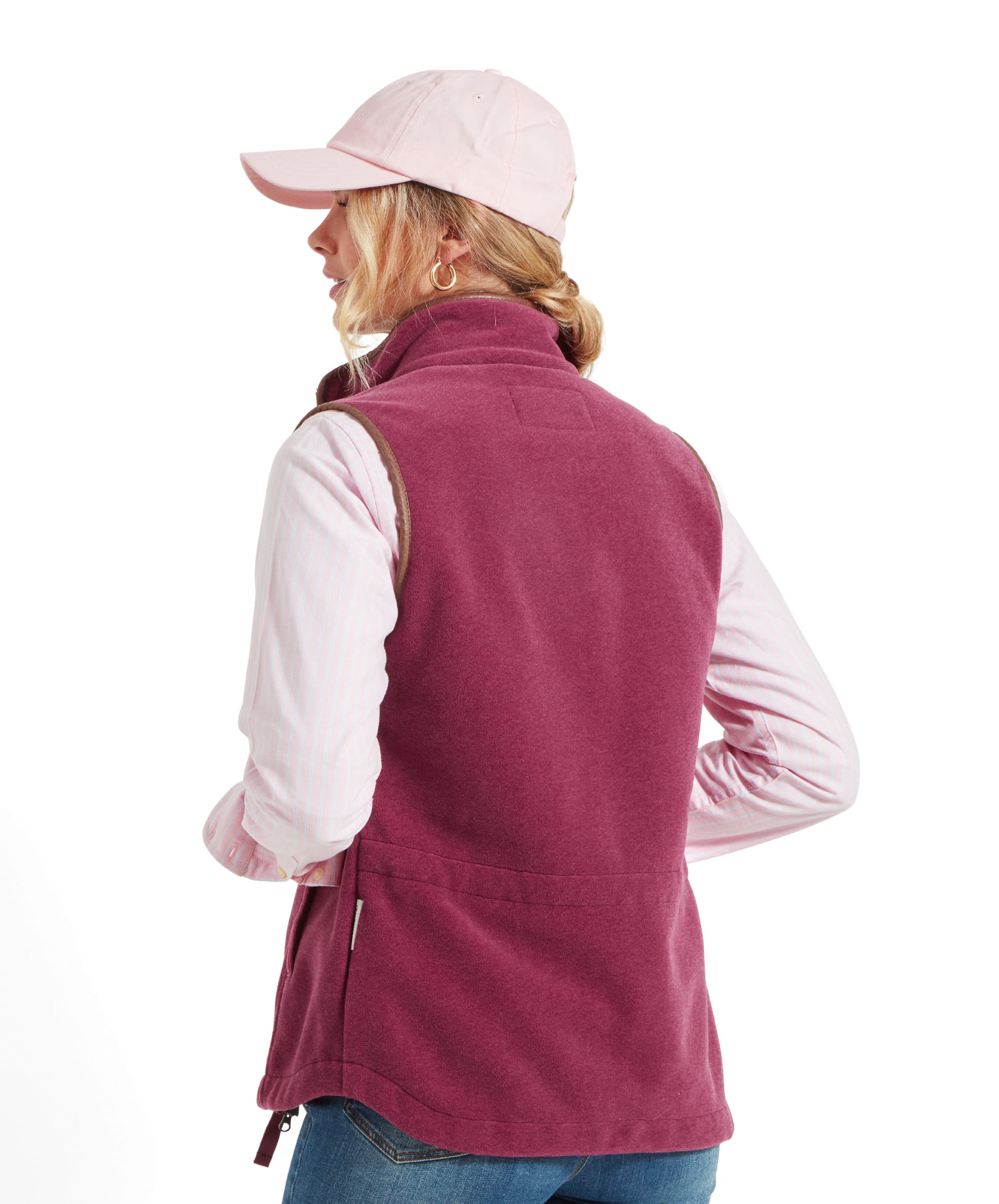 A back view of the woman wearing the Schöffel Lyndon Fleece Gilet for Women in Red. The gilet has a brown leather trim along the armholes and zipper, with a slightly fitted back design. She is also wearing a pale pink cap.