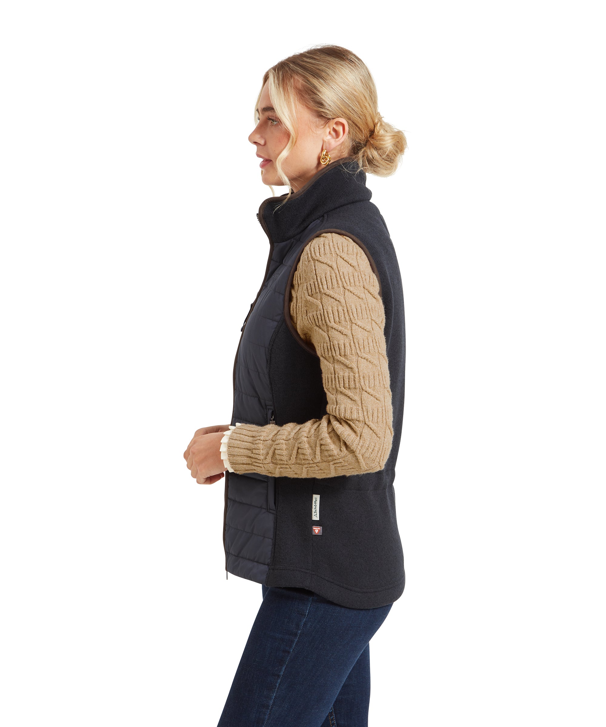 A side profile of the woman in the Schöffel Lyndon Hybrid Gilet for Women in Blue, showing the brown trim and the back elasticated waist. She is looking straight ahead with her blonde hair pulled back in a bun.