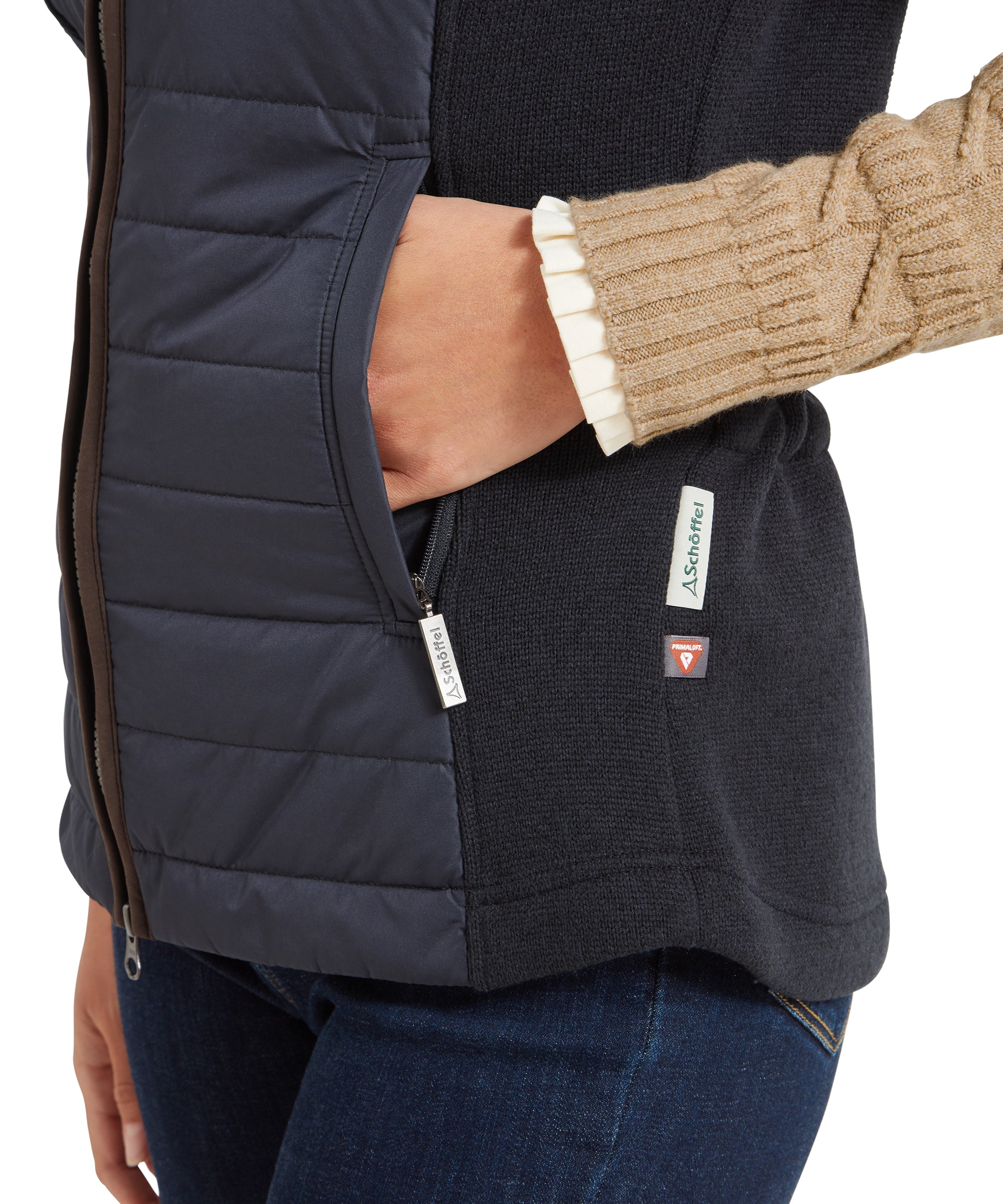 A close-up view of the pocket area of the Schöffel Lyndon Hybrid Gilet for Women in Blue, showing the brown trim, a small brand label, and the texture of the knit side panels. The woman is wearing a watch with a tan leather strap.